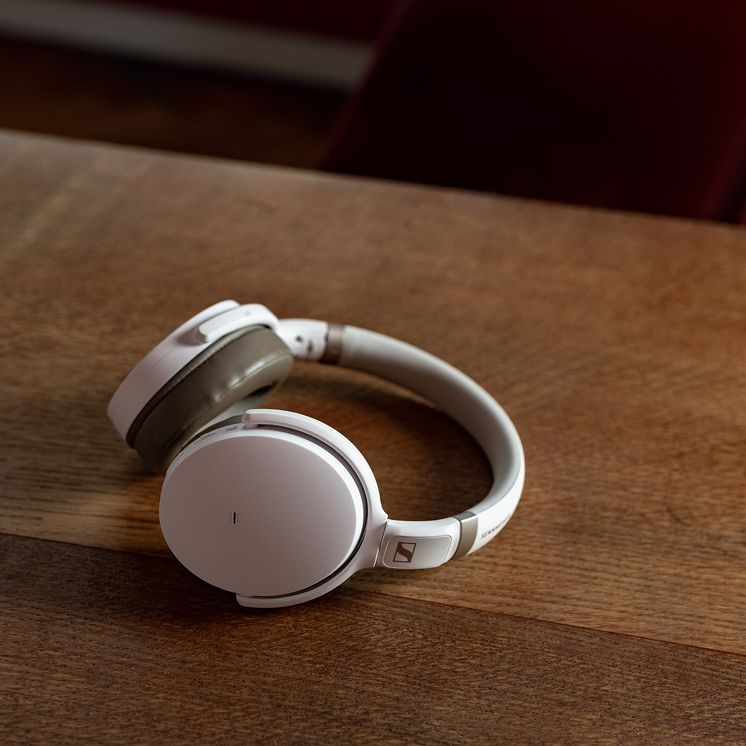 Fehér Sennheiser fejhallgató faasztalon. A fülkagylók szögben, a fejpánt ívelt.