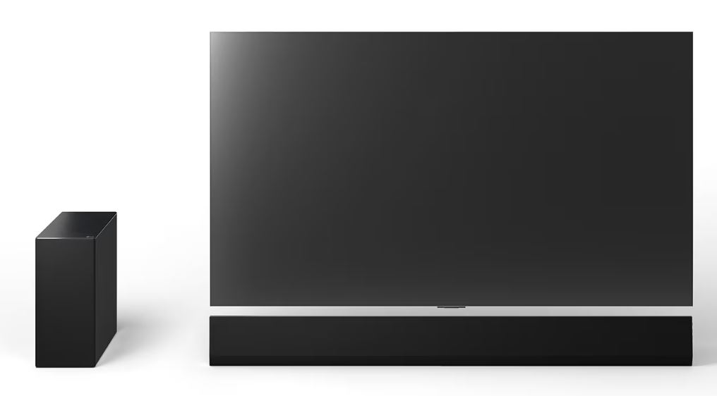 Beyaz bir yüzeyde büyük siyah bir TV ve soundbar. Solda siyah, dikdörtgen bir hoparlör duruyor.