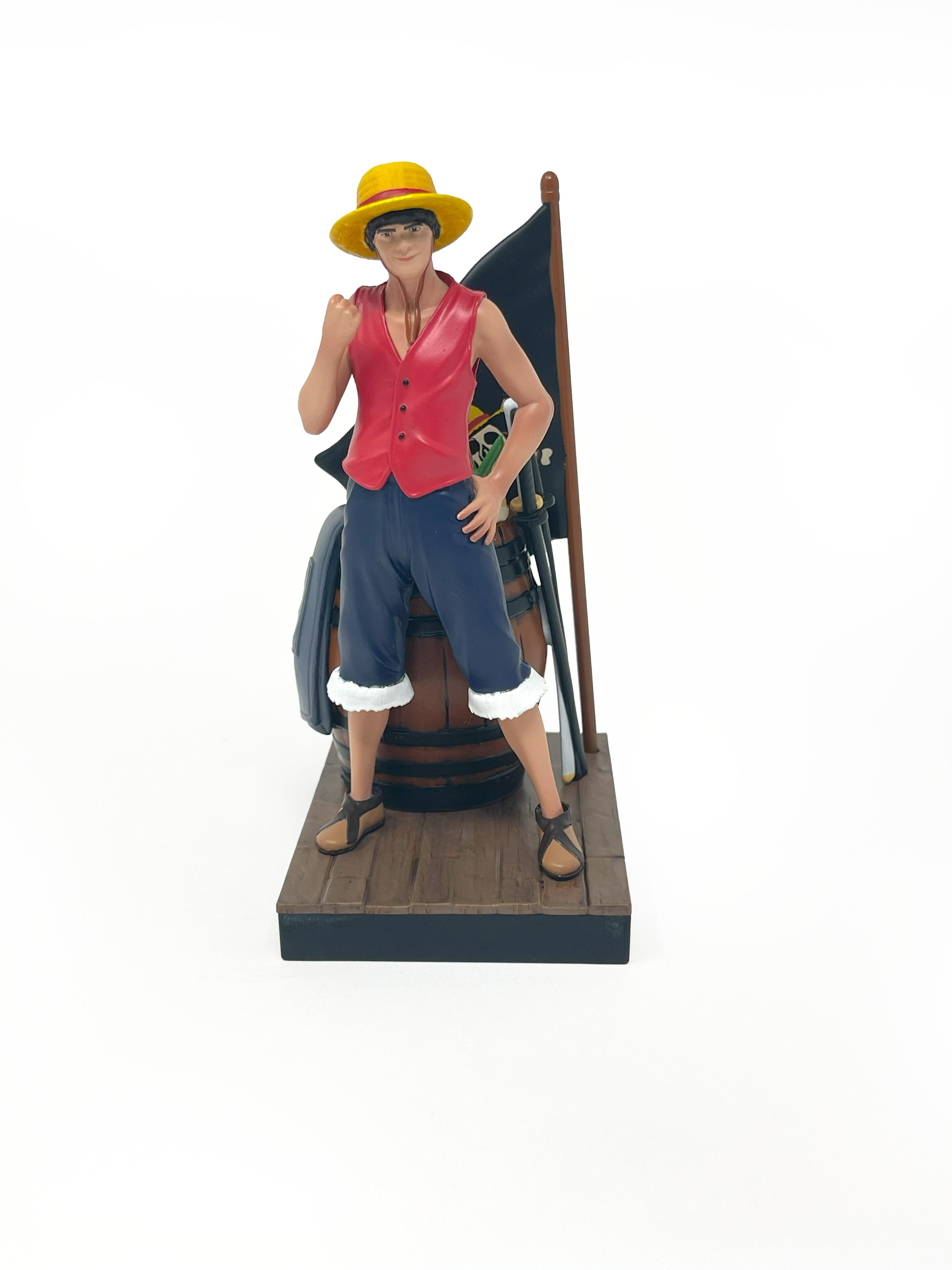 Luffy-Figur steht in der Nähe eines Fasses mit einer Flagge. Er trägt einen gelben Hut und eine rote Weste.
