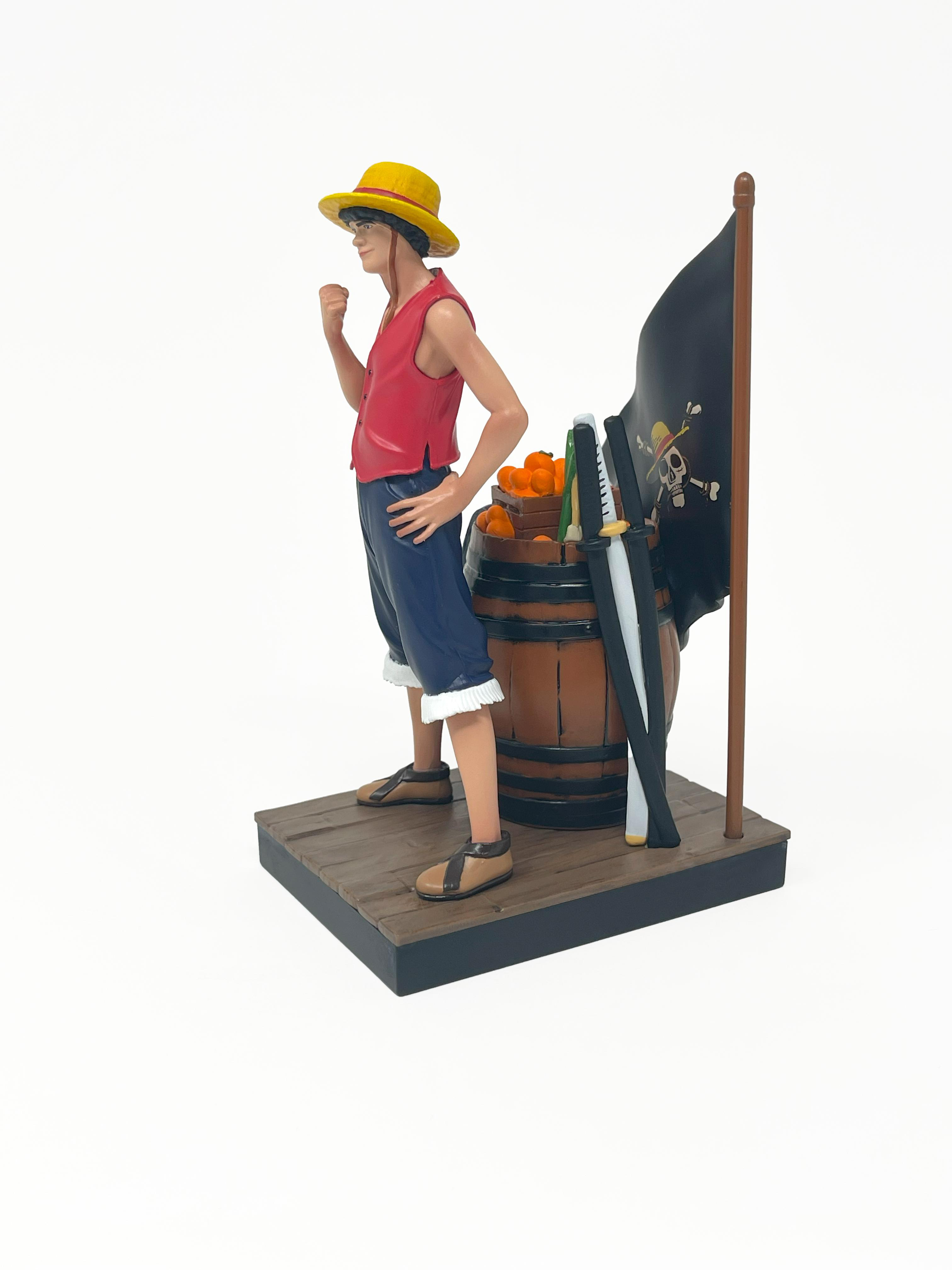 Figur einer Figur mit gelbem Hut und roter Weste, die auf einer Holzplattform steht. Im Hintergrund befindet sich eine schwarze Flagge mit Totenkopf.