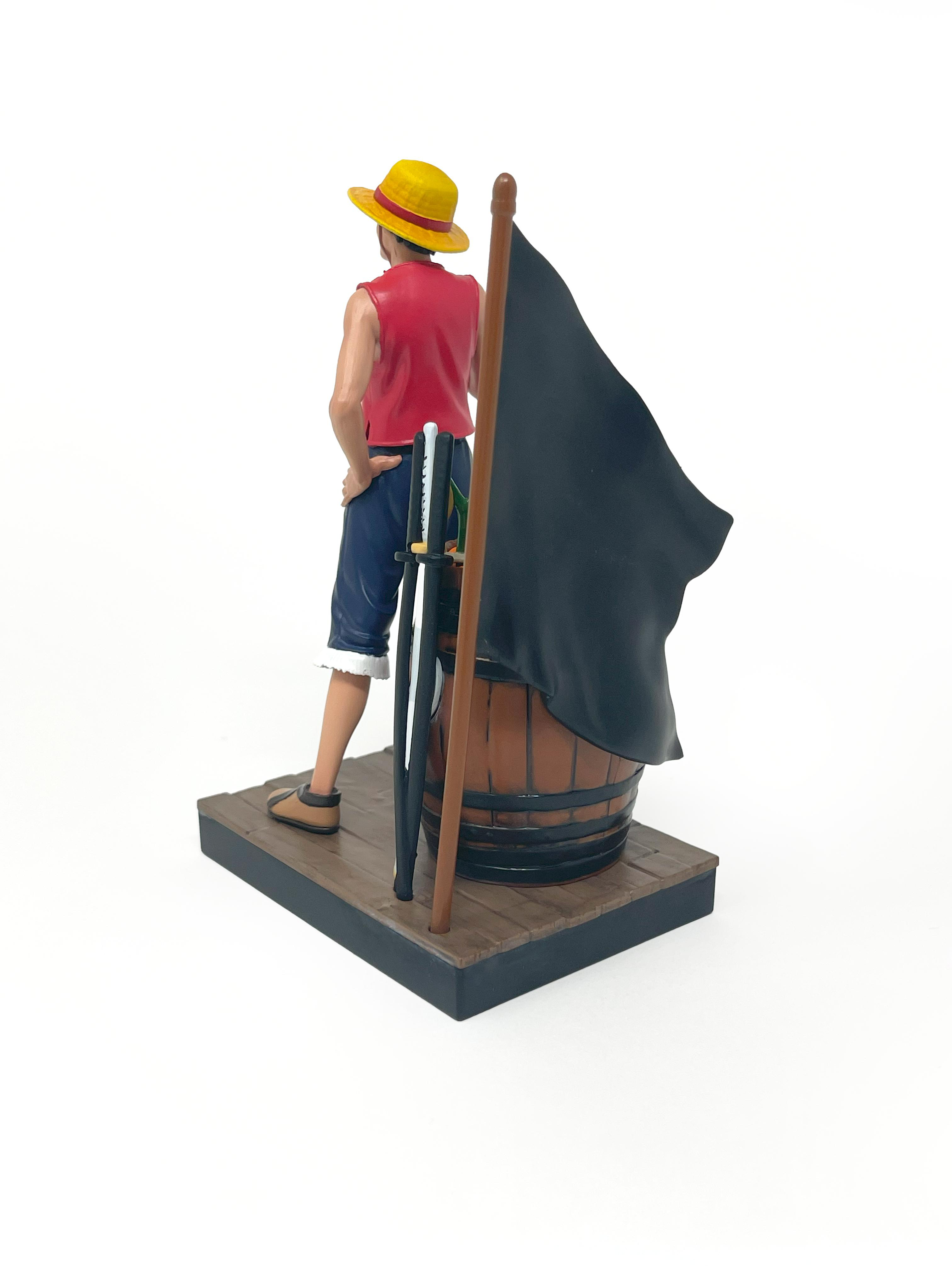 Luffy-Figur steht neben einem Fass mit einer Flagge, mit dem Rücken zur Kamera.