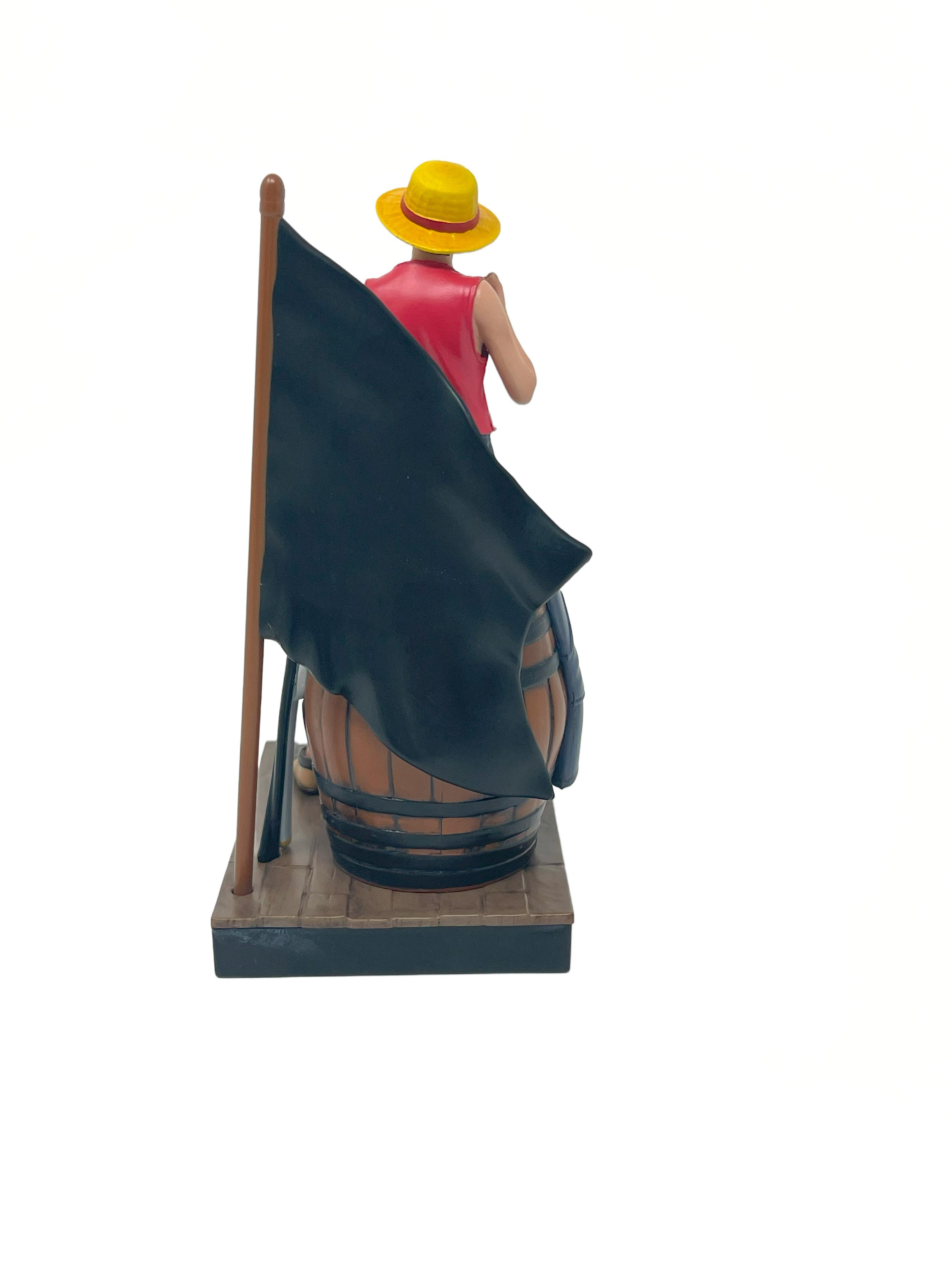 Luffy-Figur steht neben einem Fass und einer Flagge, vom Betrachter abgewandt.