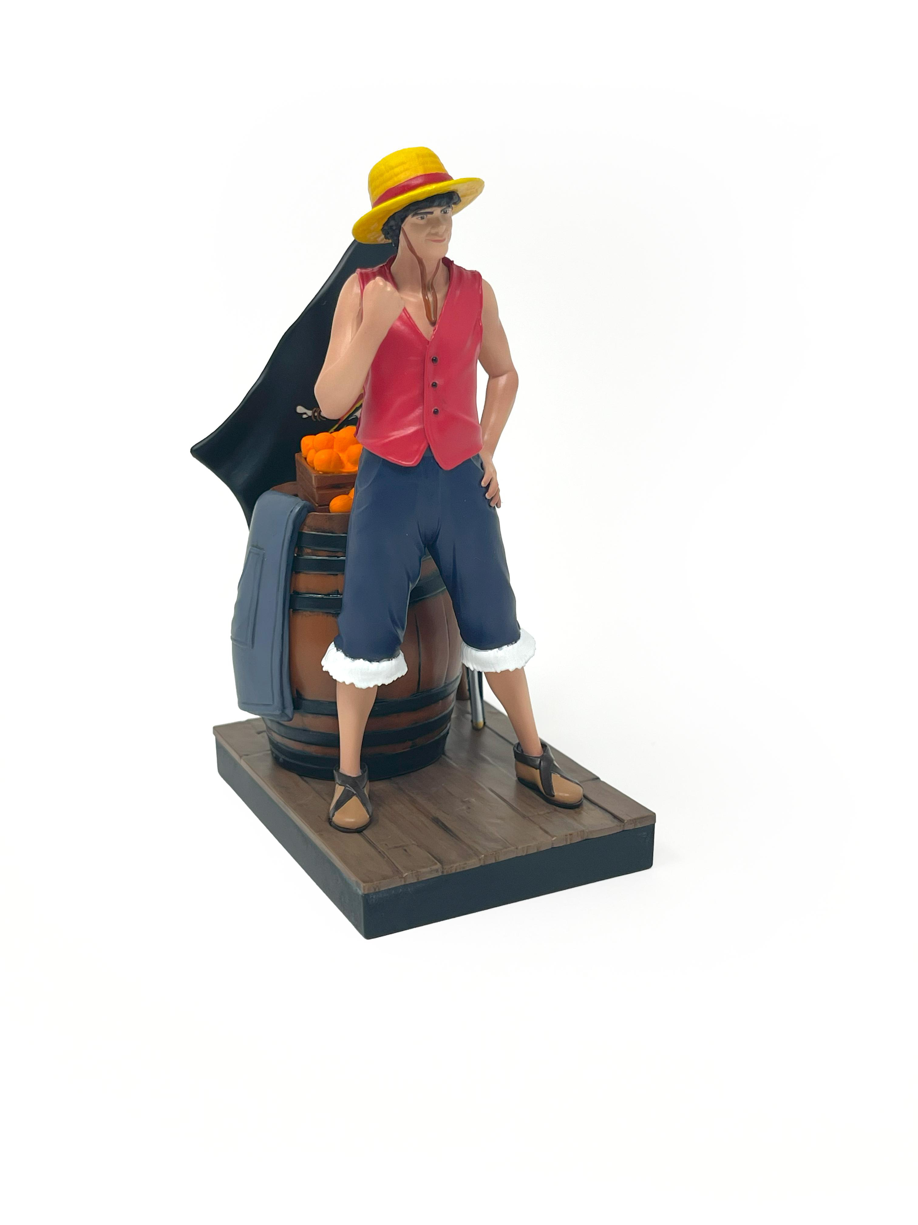 Luffy-Figur steht mit einem Fass, Orangen, einer Flagge und Schwertern. Posing mit seiner Hand.