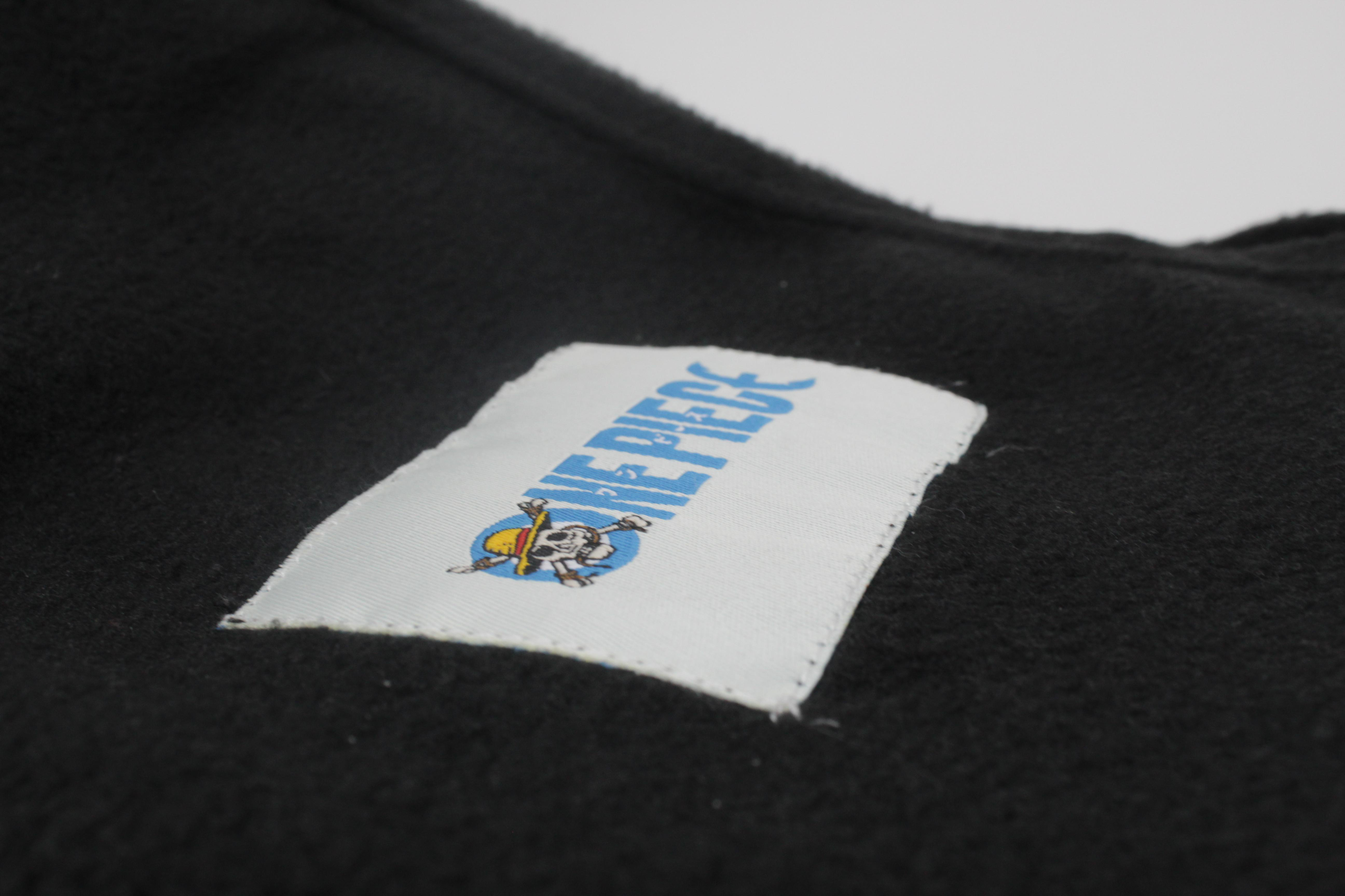 Nahaufnahme eines weißen Etiketts mit dem One Piece-Logo auf schwarzem Stoff.