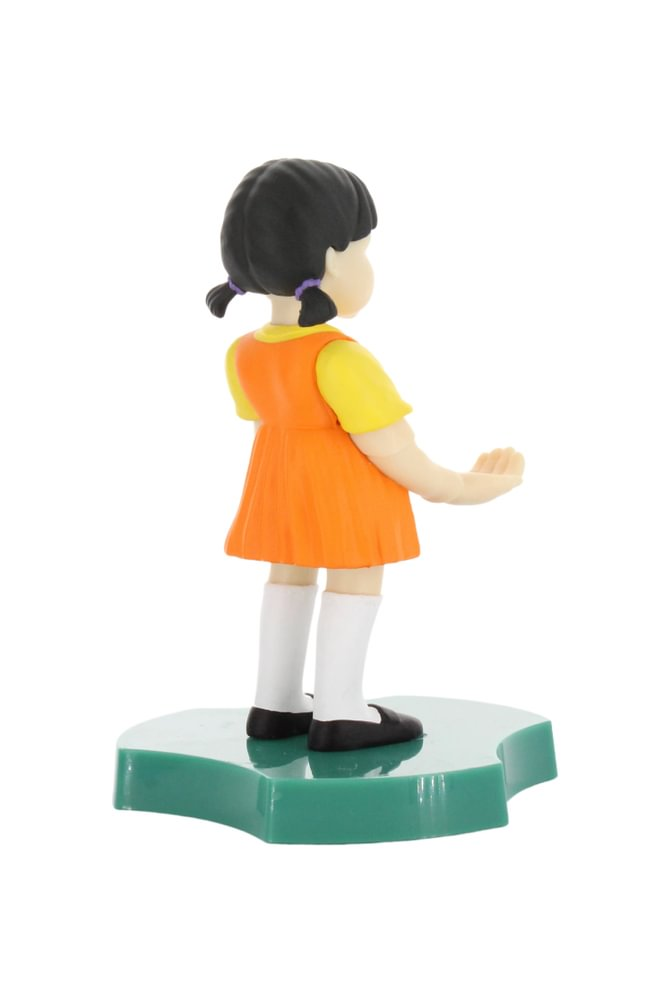 Figur eines Mädchens aus Squid Game, in orangefarbenem Kleid und gelbem Hemd, auf grüner Basis.