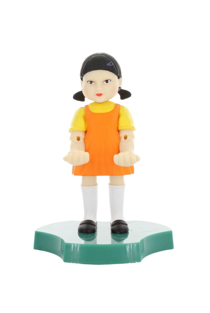 Squid Game Mädchen-Figur. Orangefarbenes Kleid, gelbes Hemd, Zöpfe, auf grüner Basis.
