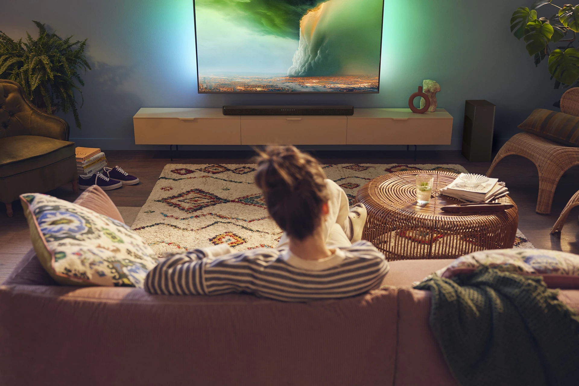 Persona ve la TV mostrando escena de paisaje, con sofá, alfombra y mesa de centro.