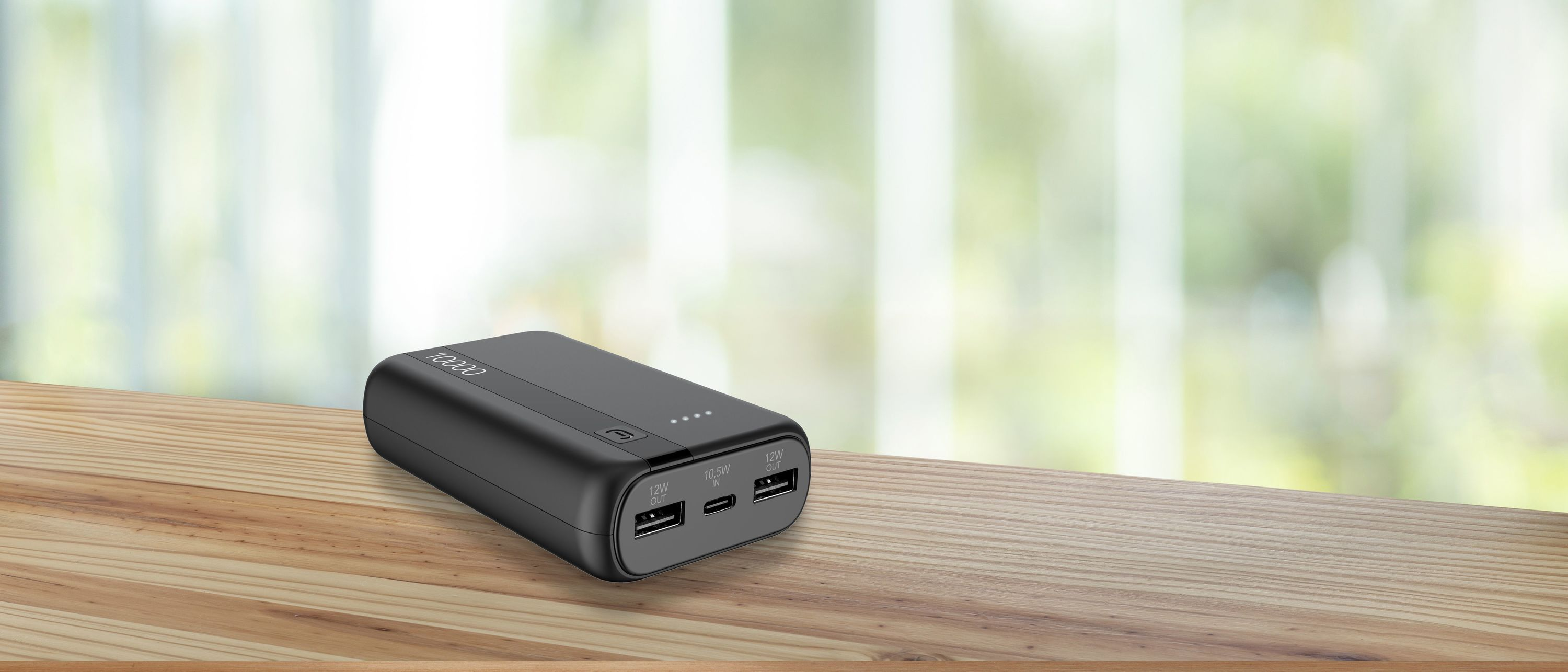 Ahşap masada siyah powerbank. Bulanık yeşil ve beyaz arka plan. USB bağlantı noktalarına sahip.