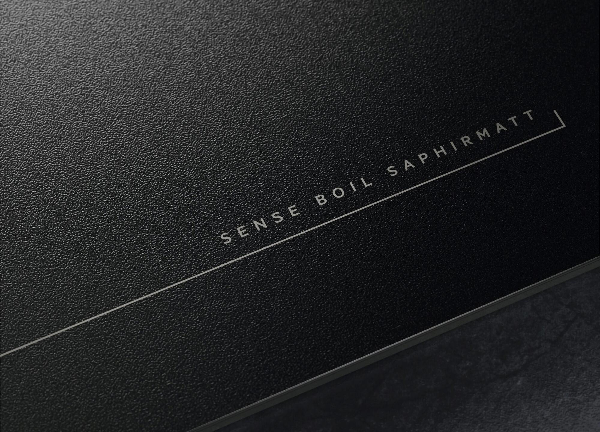 Nahaufnahme eines schwarzen Kochfelds. Der Text „SENSE BOIL SAPHIRMATT“ ist auf der Oberfläche gedruckt.
