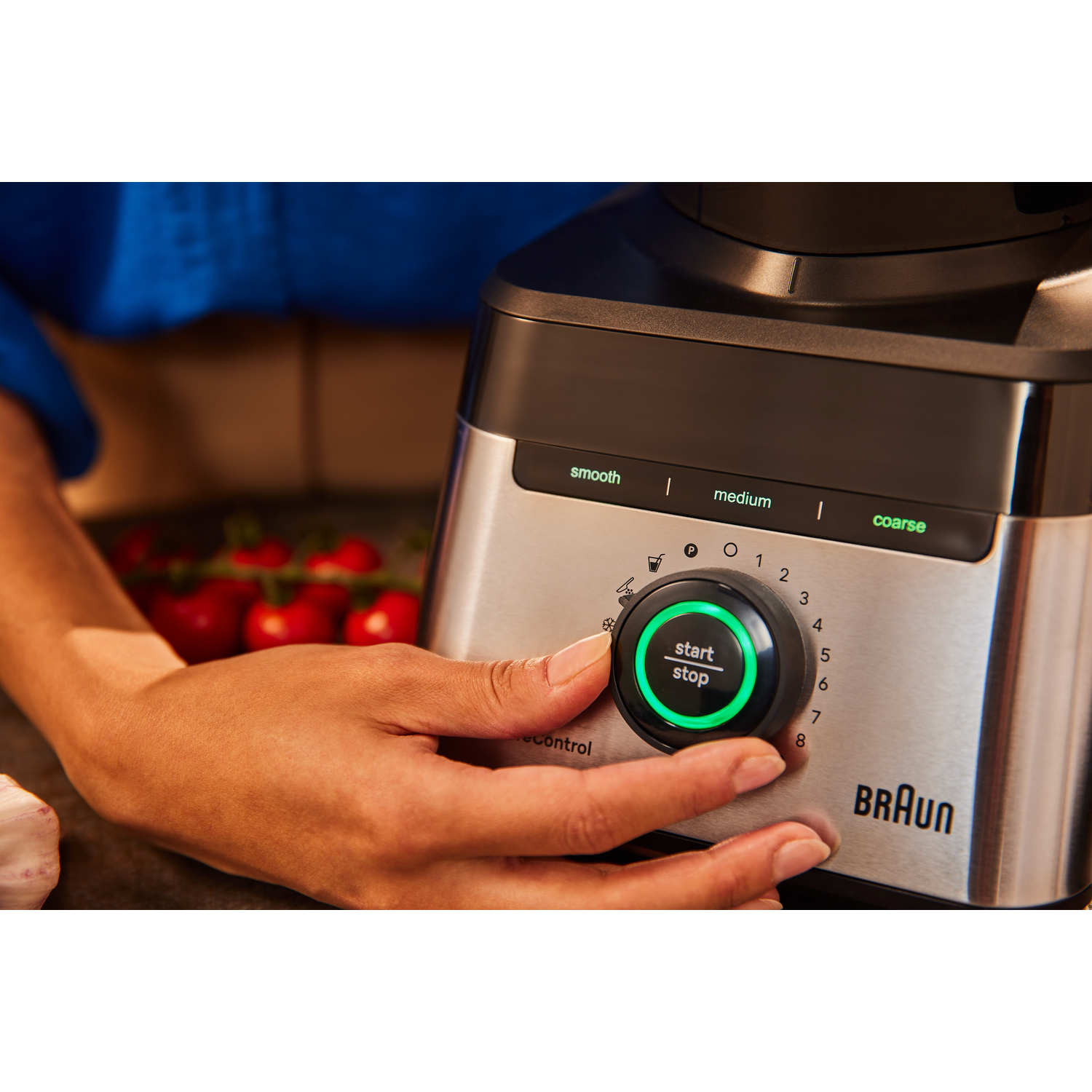 A person's hand on a Braun blender, with a green light on the start/stop button.