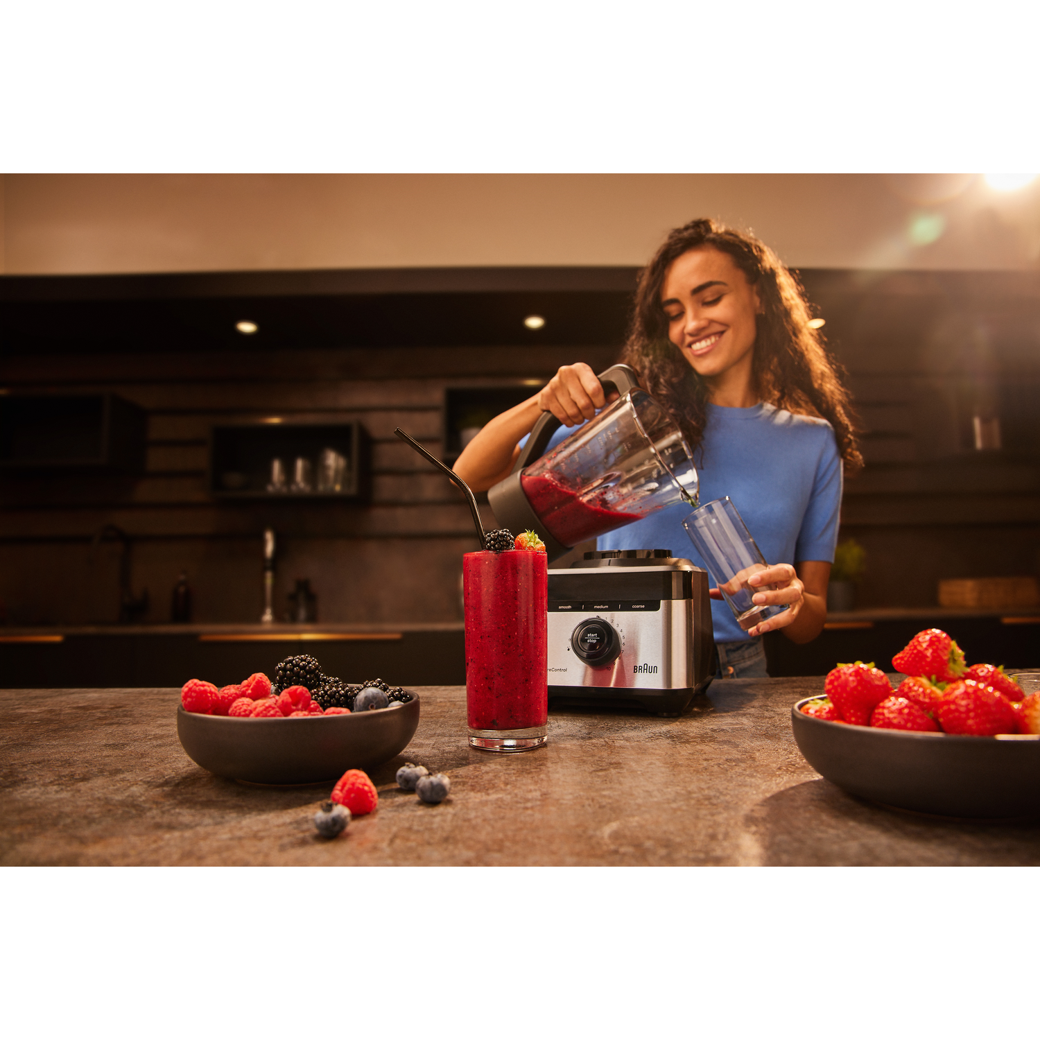 Woman pours a red smoothie from a blender into a glass.
