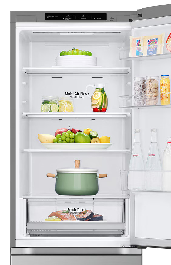 Otwarta lodówka wypełniona jedzeniem. Zawiera owoce, napoje i warzywa. Garnek stoi na półce.