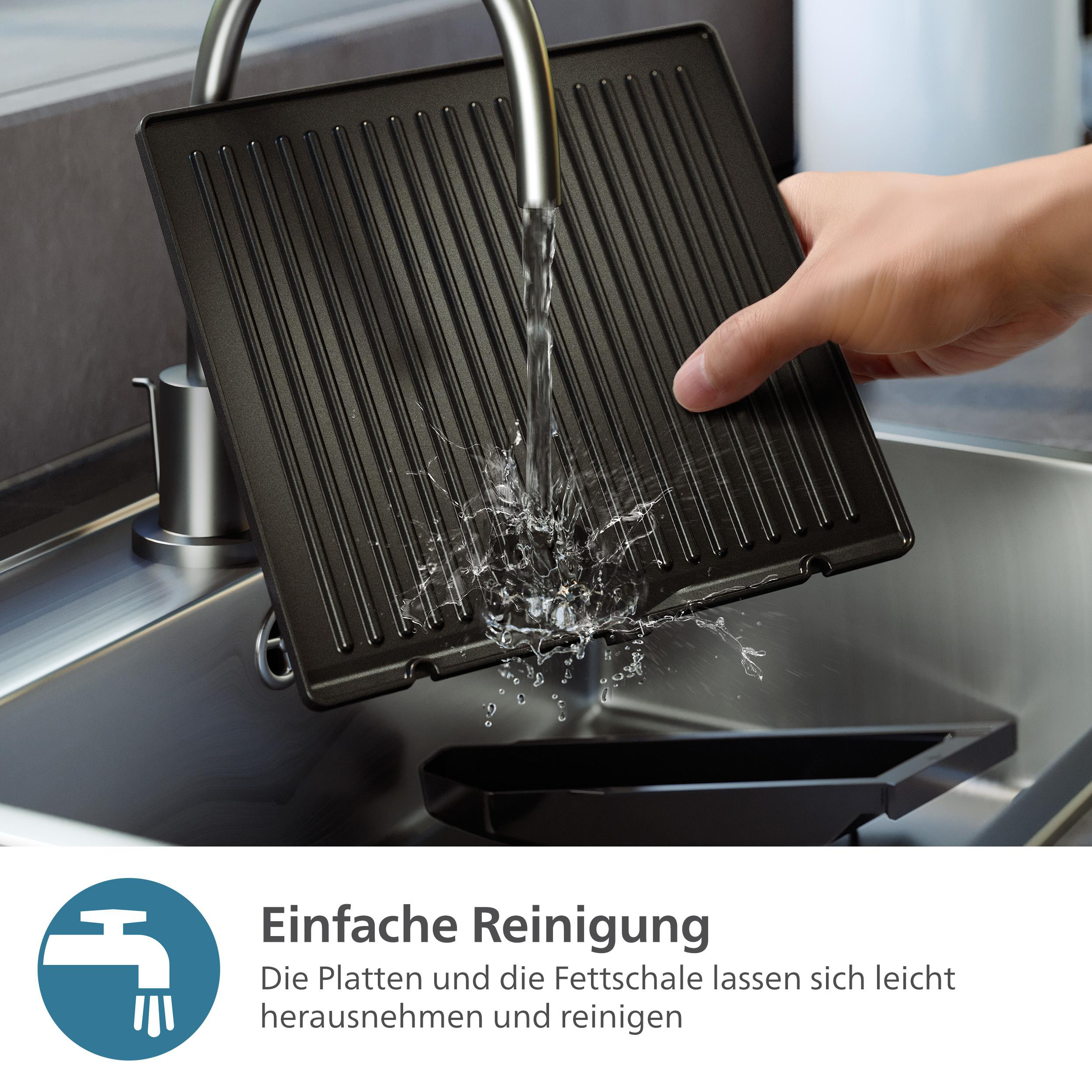 Eine Hand wäscht eine Grillplatte. Wasser wird auf die schwarze Platte in einem Waschbecken gespritzt.