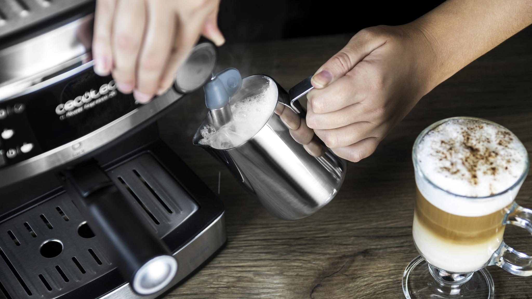 Una persona vierte leche en una jarra plateada. Una cafetera está en el fondo.