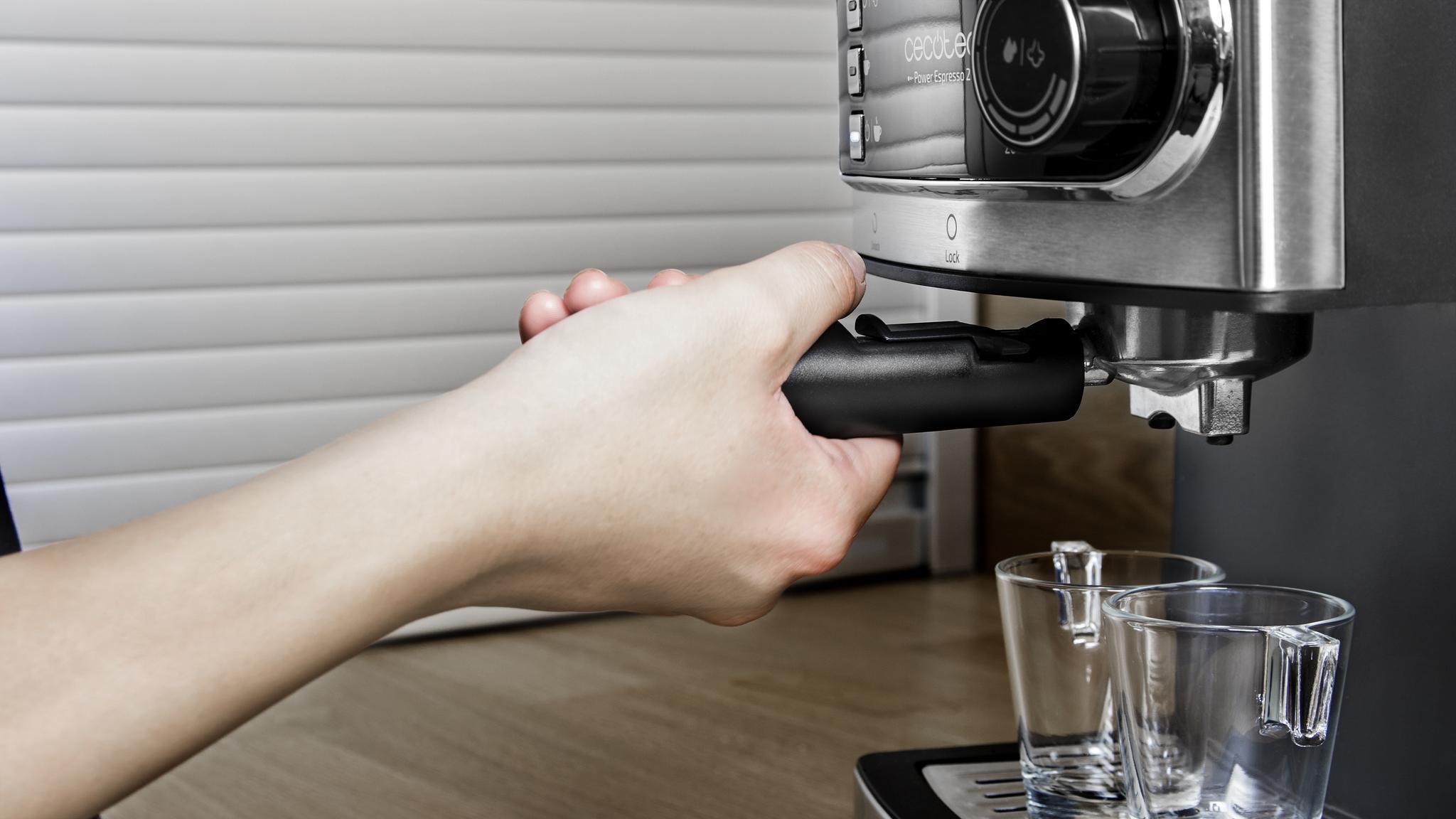 Una persona sosteniendo un portafiltro negro, preparando espresso. Dos vasos están en el mostrador.