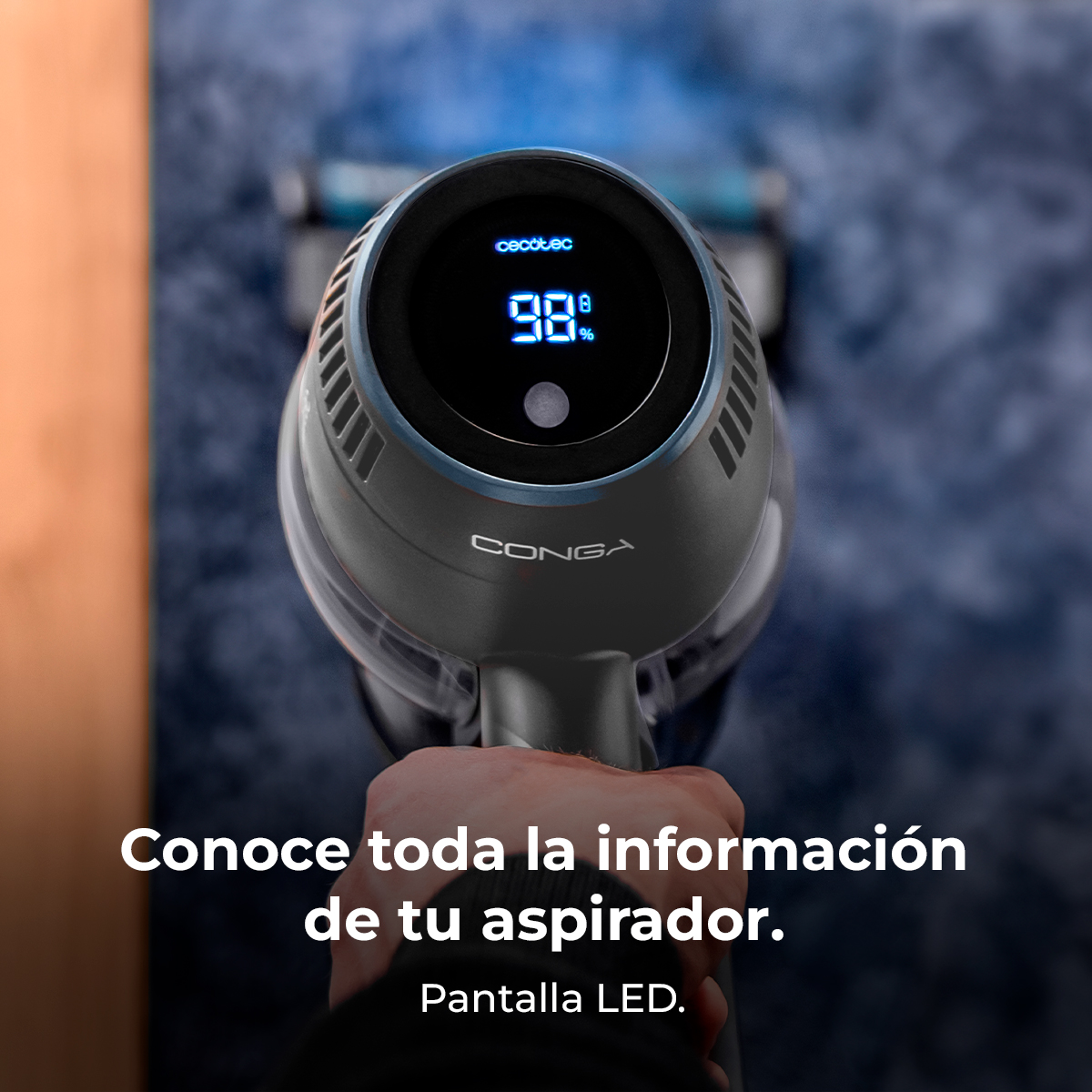 Una mano sostiene una aspiradora negra y gris; pantalla LED muestra 98%.