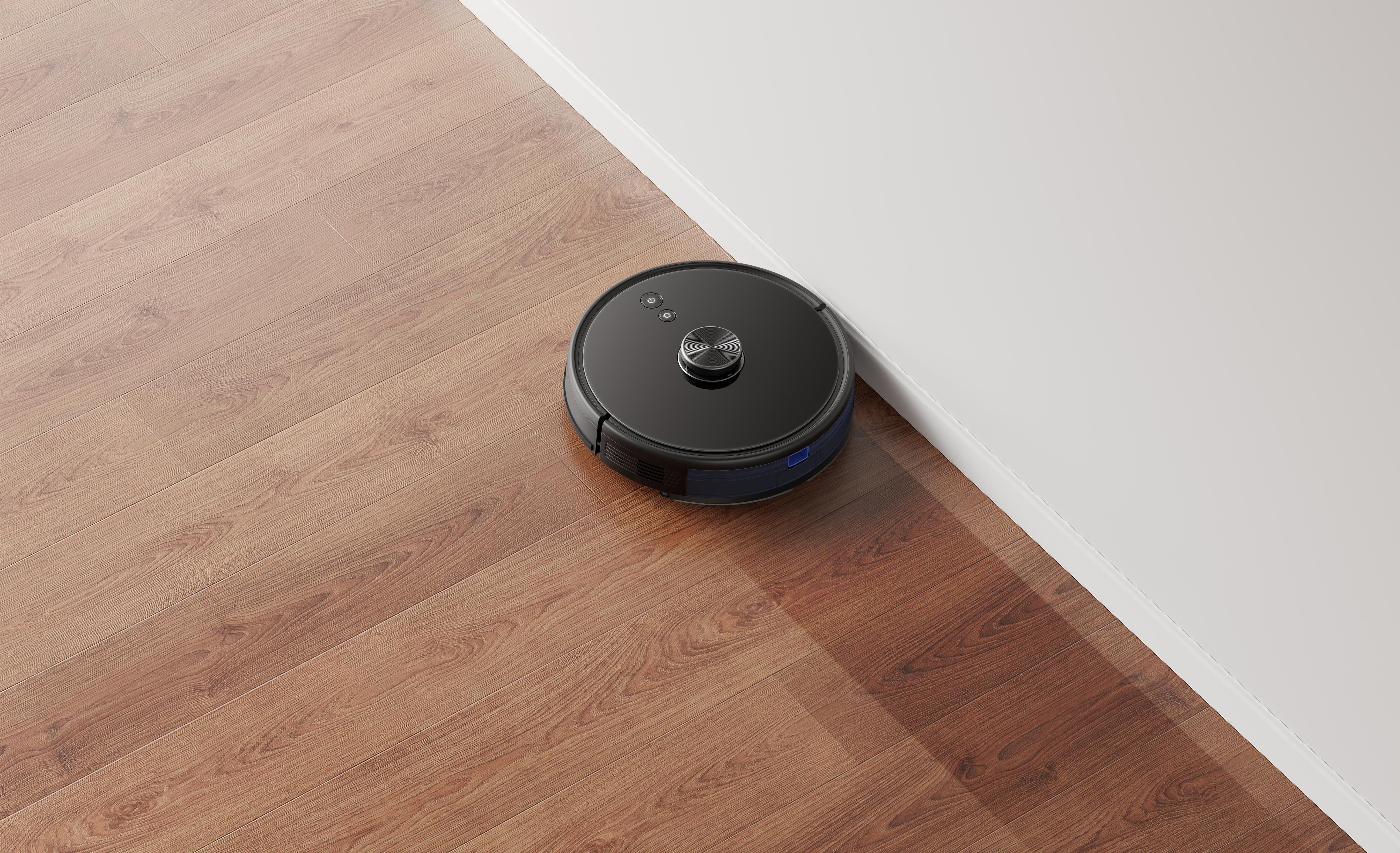 Ein schwarzer Roboter-Staubsauger auf einem Holzboden in der Nähe einer weißen Wand. Der Boden ist braun mit Holzmaserung.