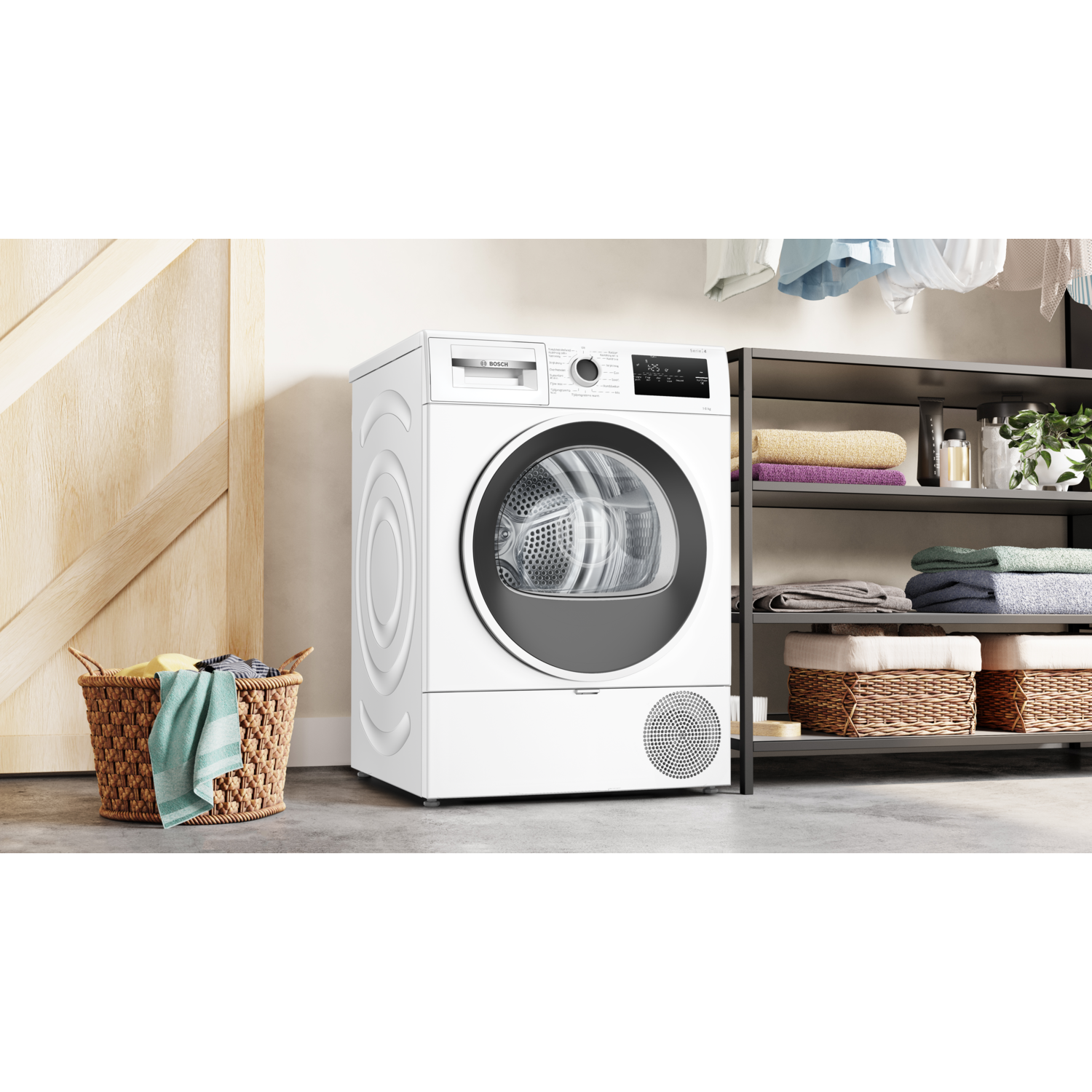 Witte wasmachine in wasruimte, deur gesloten. Mand en planken met kleren in de kamer.