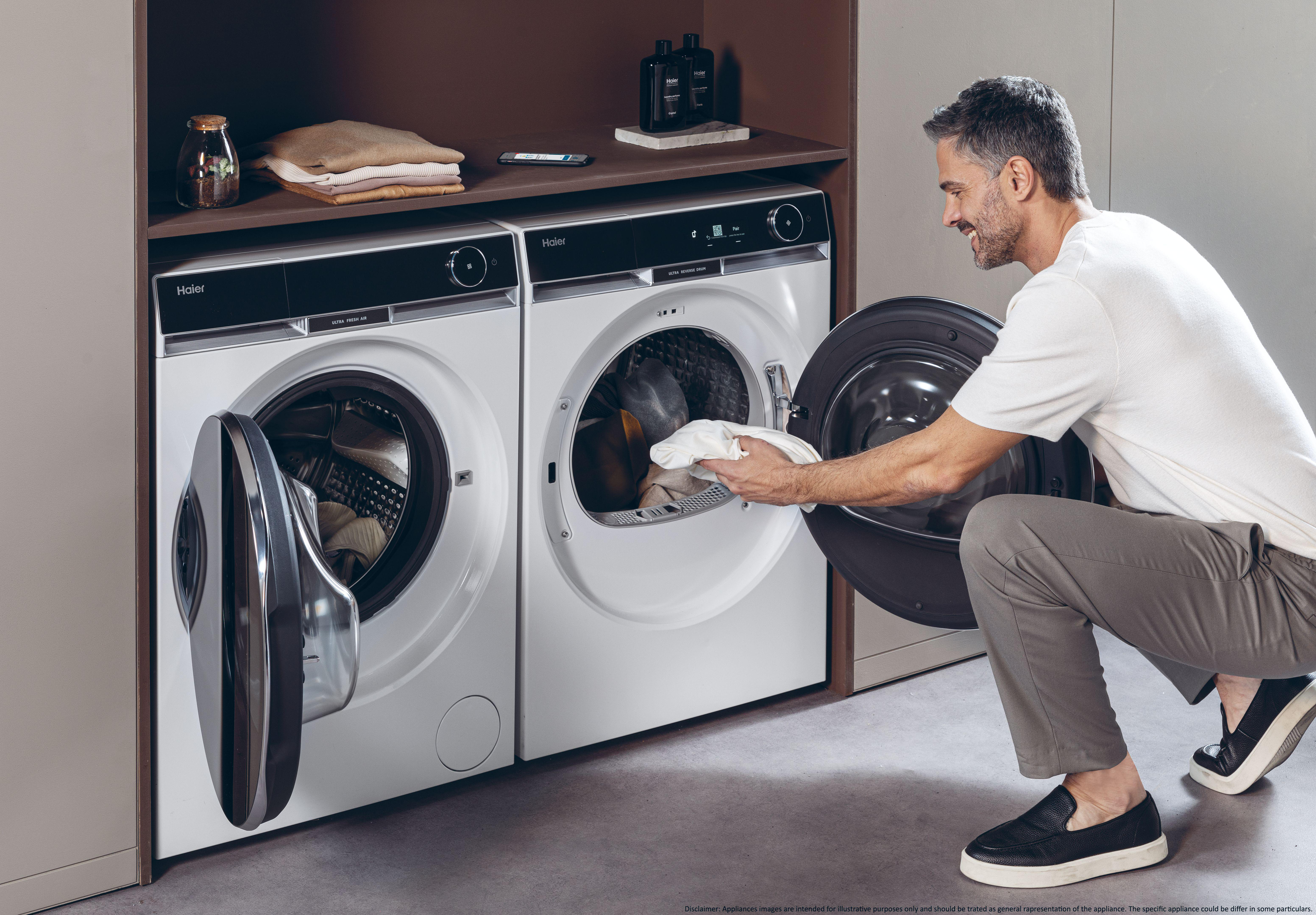 Ein Mann, der Kleidung in eine Haier Waschmaschine lädt, mit einem passenden Trockner daneben.