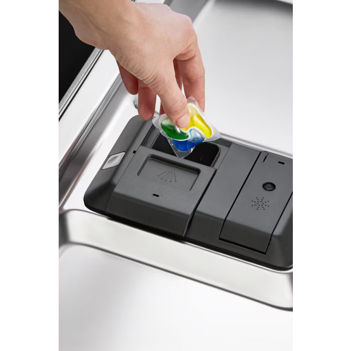Eine Hand legt einen Geschirrspülertab in einen Spender in einem Edelstahl-Geschirrspüler.