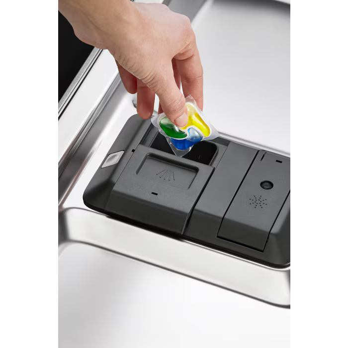 Eine Hand legt eine farbenfrohe Waschmittelkapsel in den Spender einer Spülmaschine.