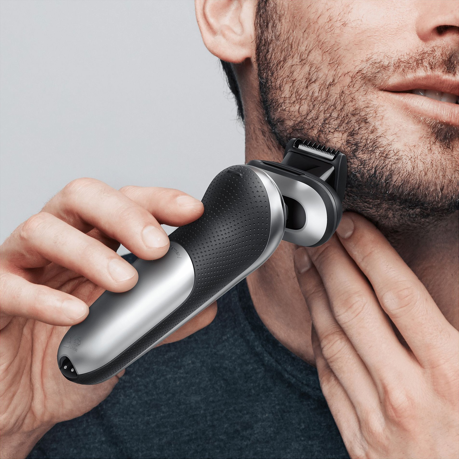 Un uomo si rade la barba con un rasoio elettrico, il suo viso nell'inquadratura.