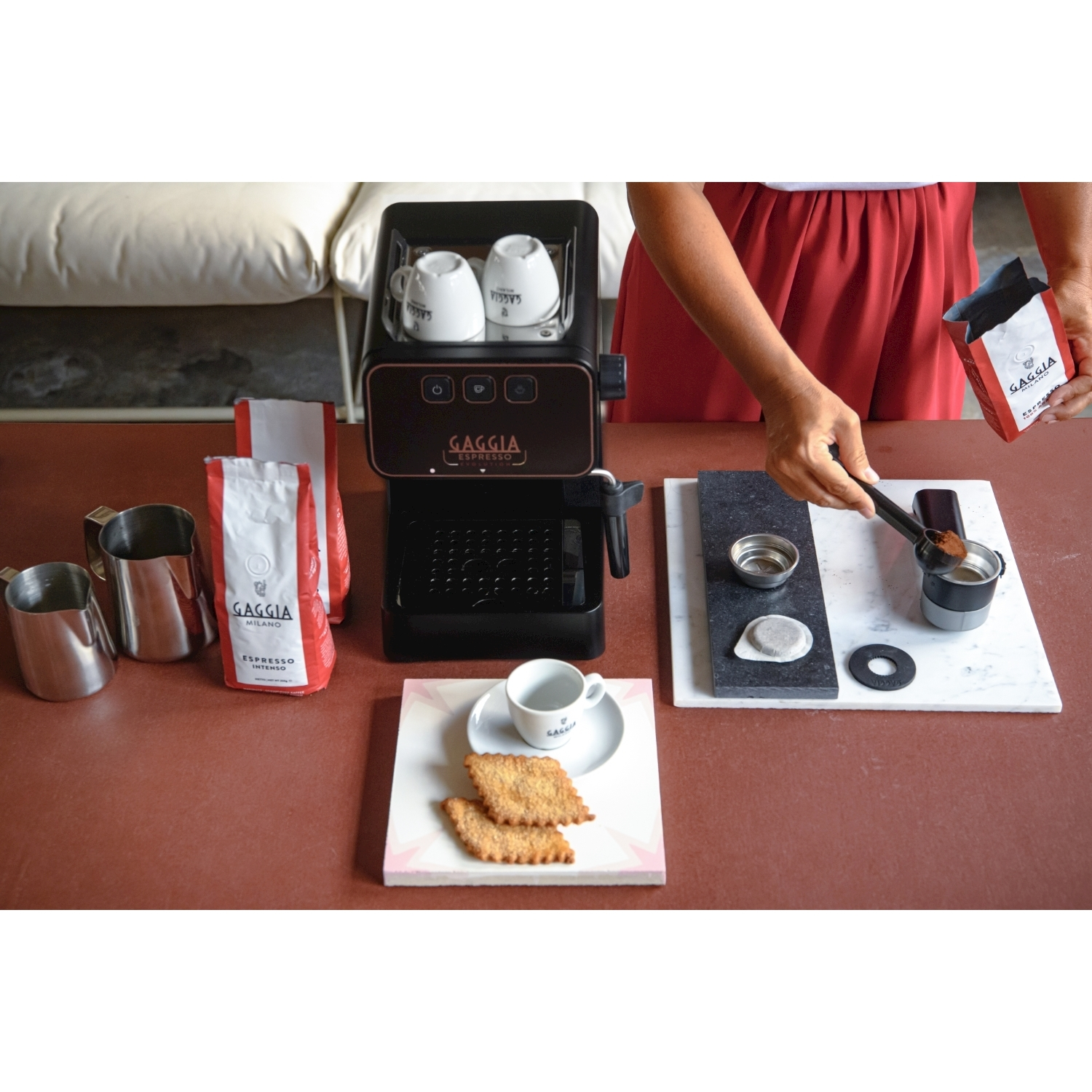 Macchina per caffè espresso con tazze, biscotti e sacchetti di caffè su un tavolo.