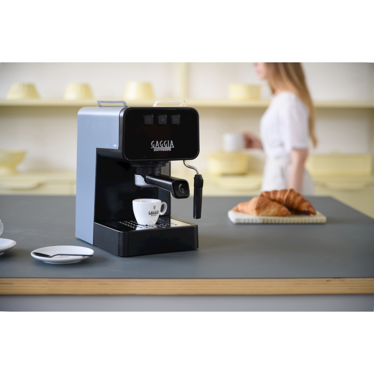 Una macchina per l'espresso con una tazza, croissant su un piatto e una persona sullo sfondo.