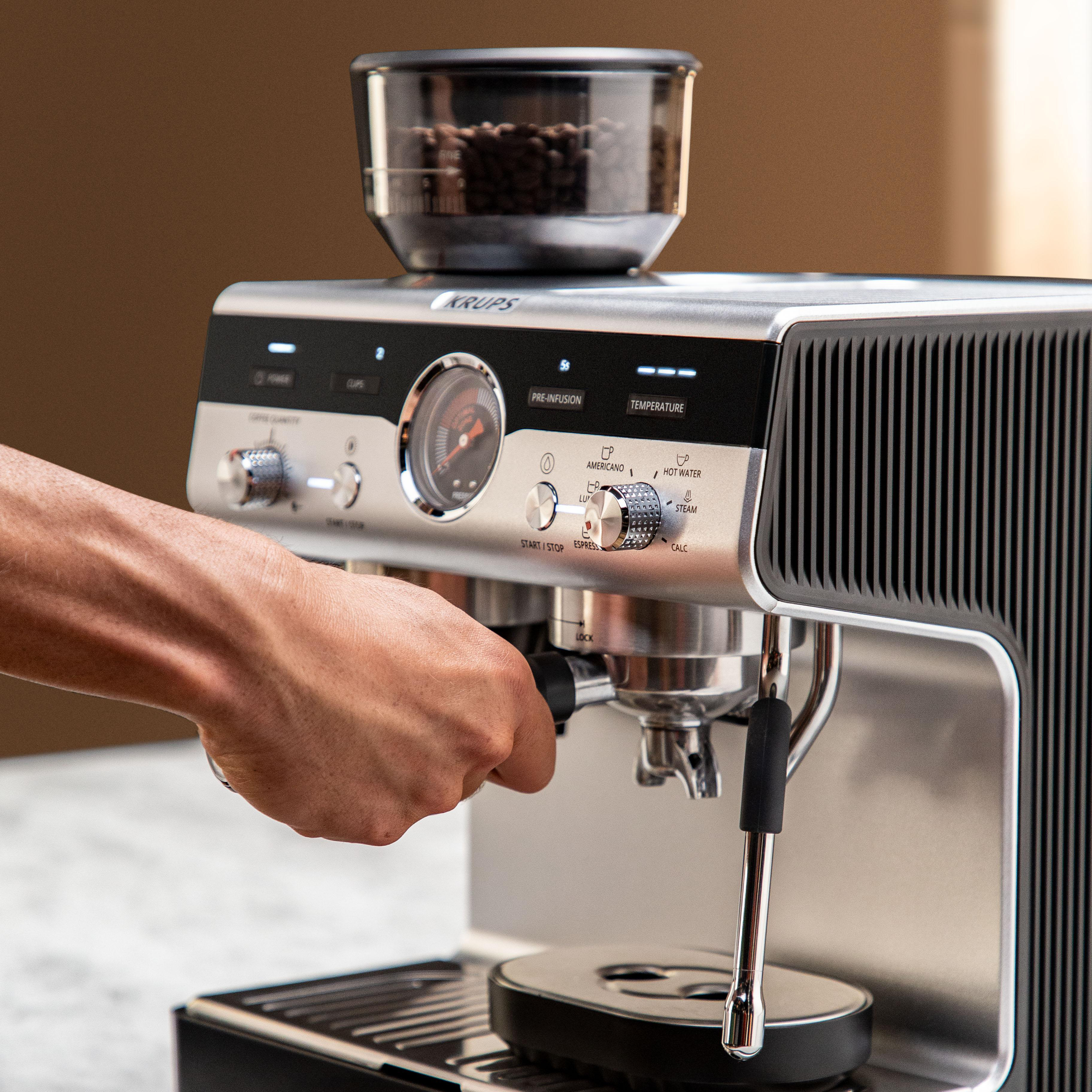 Eine Hand setzt den Siebträger in eine Krups Espressomaschine ein, Kaffeebohnen im Behälter.