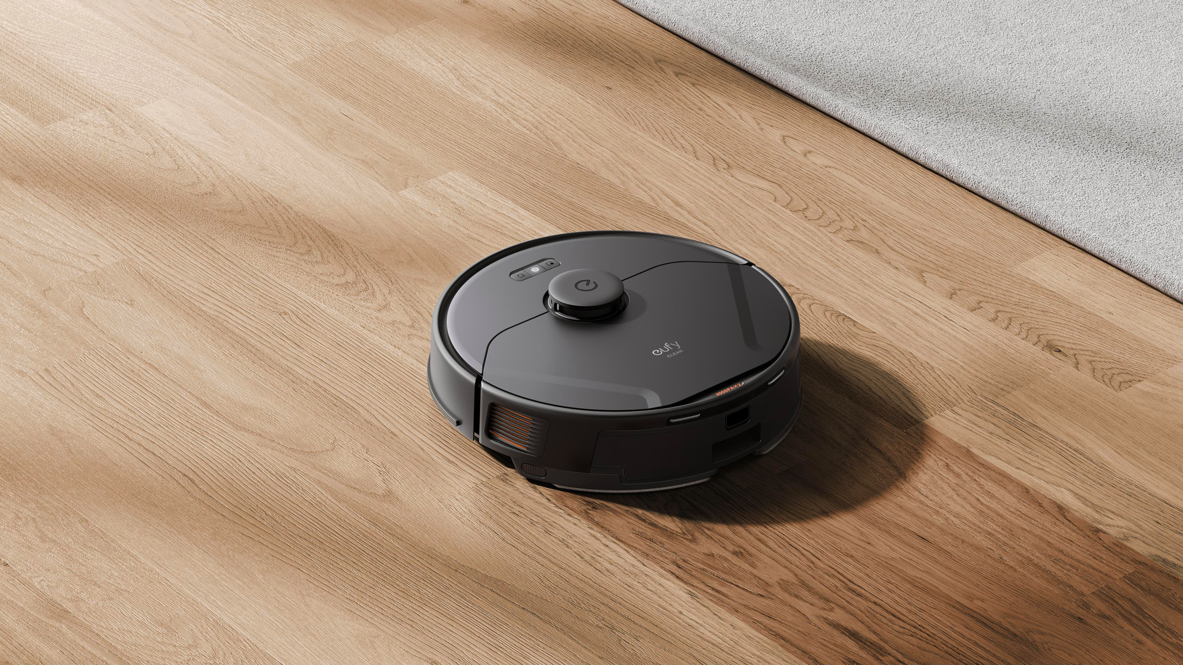 Ein schwarzer Eufy-Roboterstaubsauger auf einem Holzboden in der Nähe eines hellgrauen Teppichs.