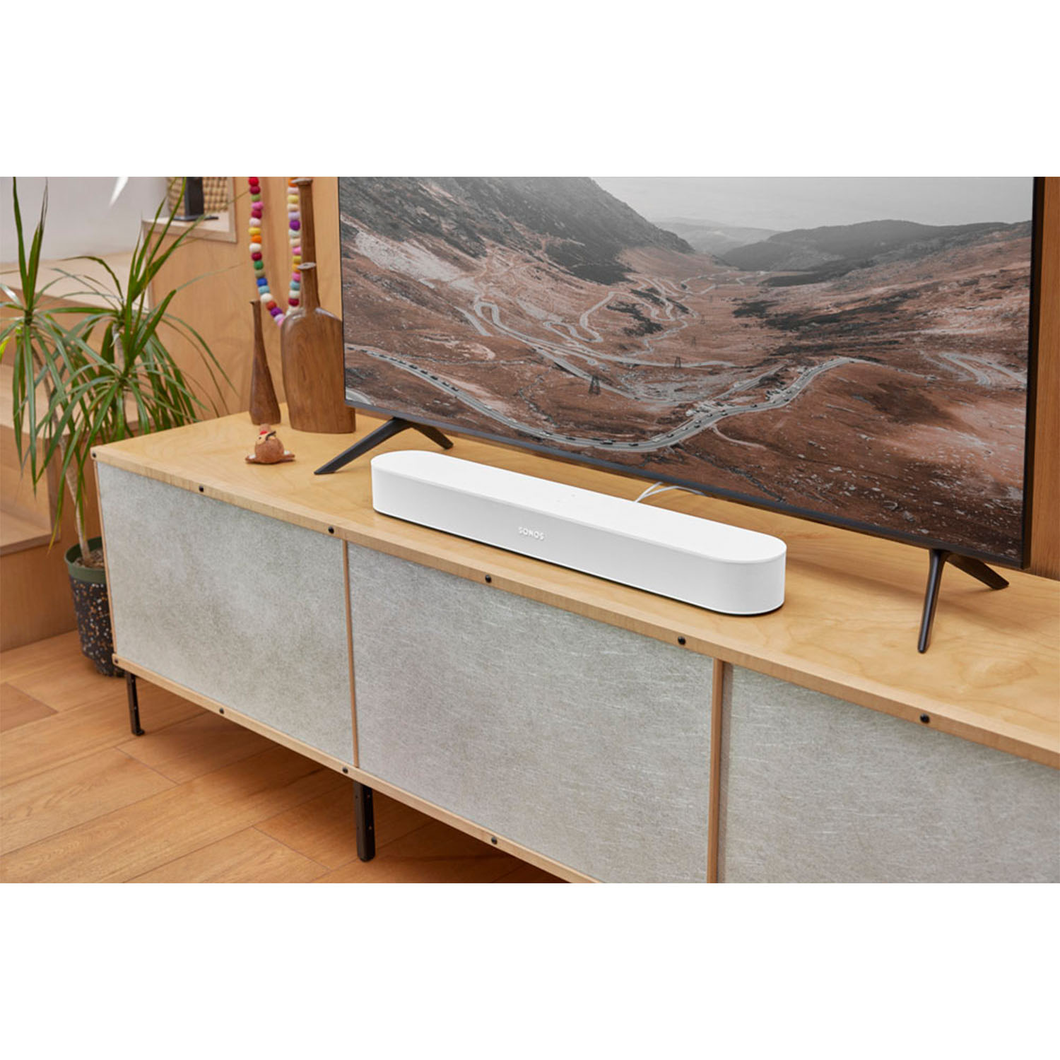 Soundbar bianca di fronte a una TV. La TV è su un mobile in legno. Lo sfondo è una parete strutturata.