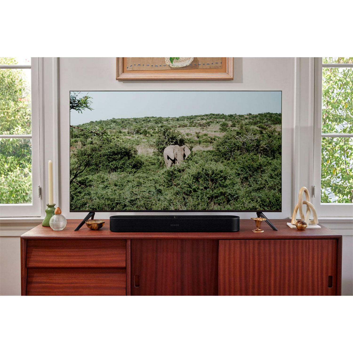 Una soundbar nera è posizionata su un mobile in legno di fronte a un televisore. Lo sfondo mostra un paesaggio.