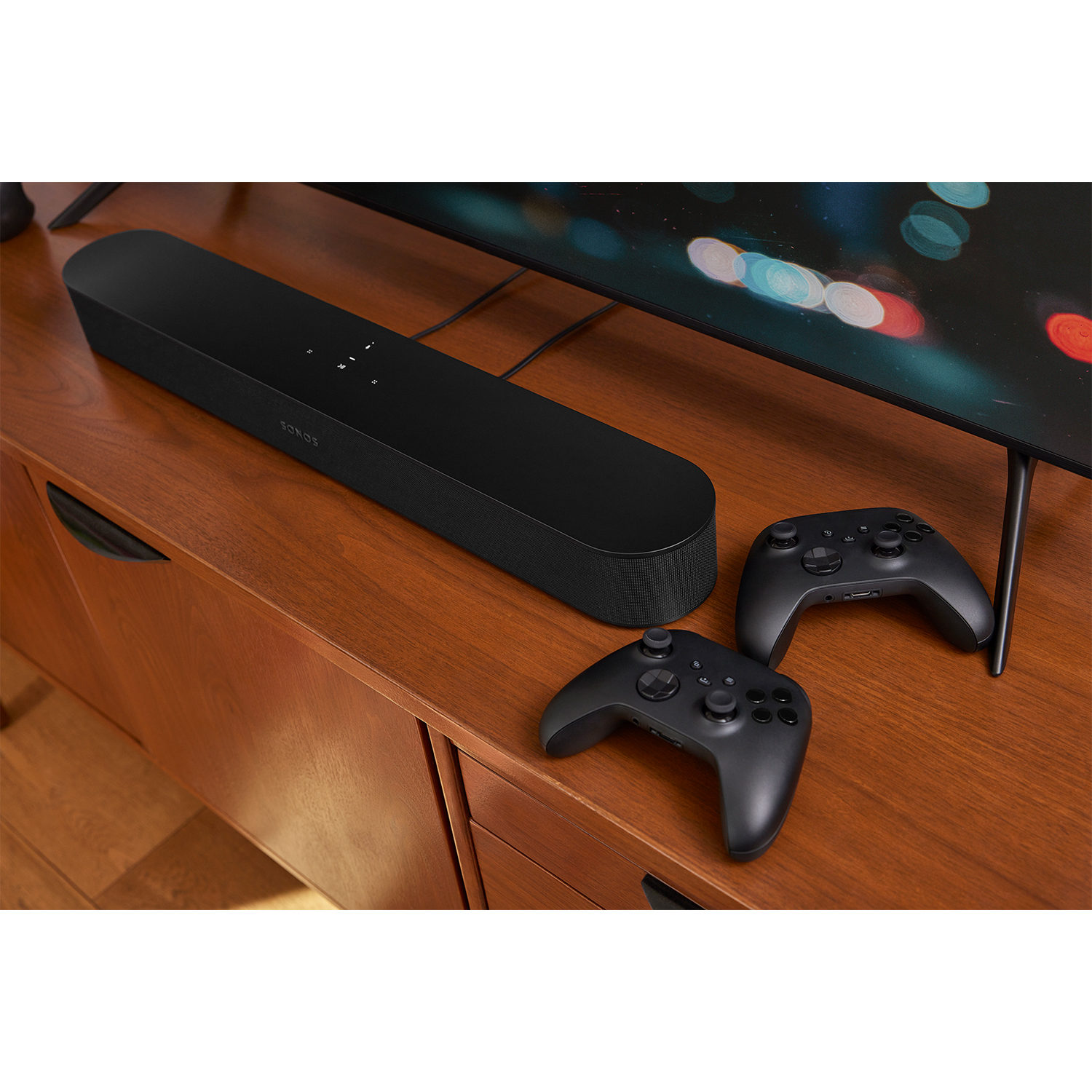 Una soundbar nera con una TV e due controller di gioco neri su una superficie in legno.
