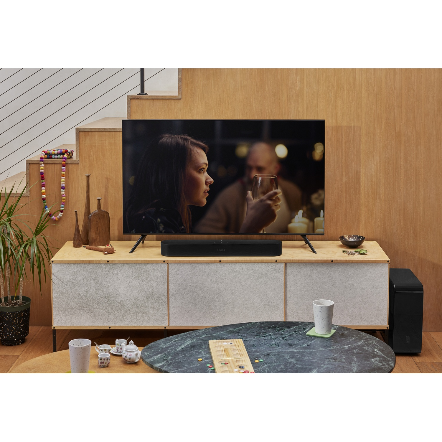 Scena del soggiorno con TV, soundbar, subwoofer e persone sfocate.