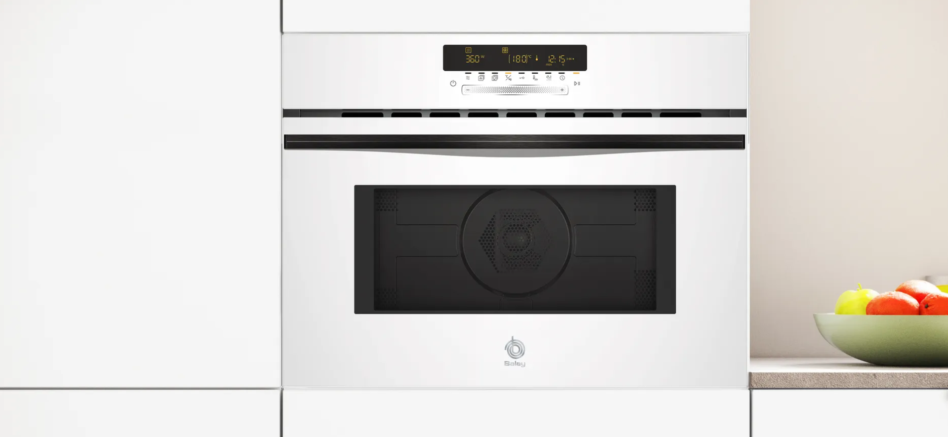 Horno empotrado blanco con pantalla digital, junto a un armario blanco y un frutero.