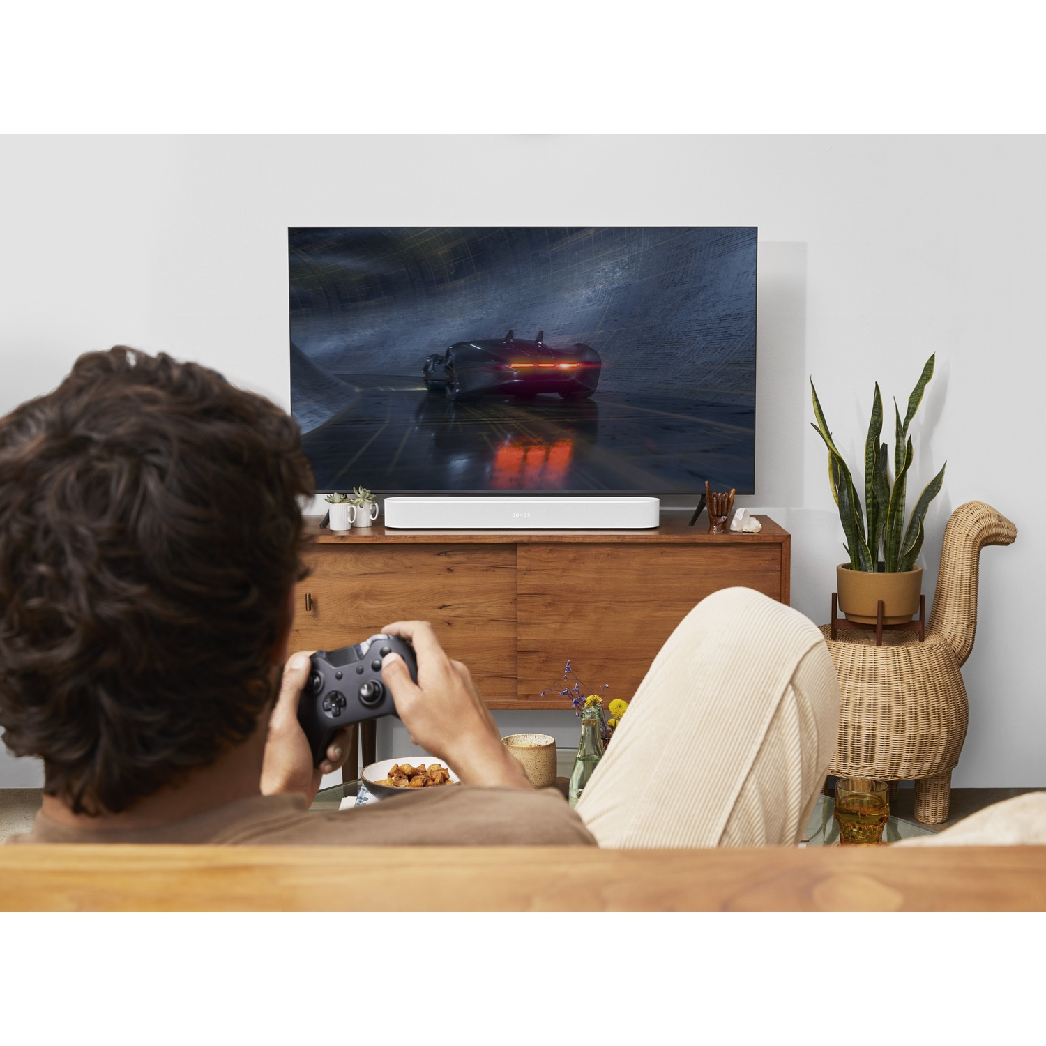 Persona che gioca ai videogiochi su grande TV con soundbar e arredamento.