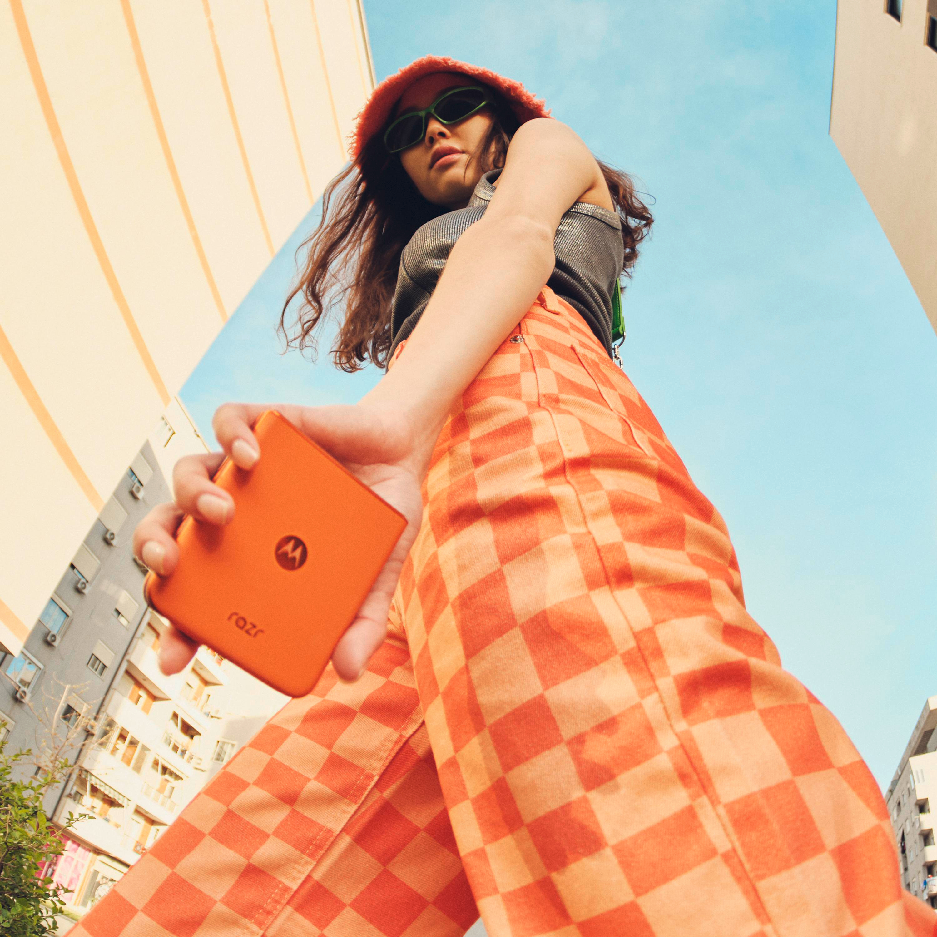 Eine Person in orangefarbener Hose und grünem Oberteil hält ein Telefon.