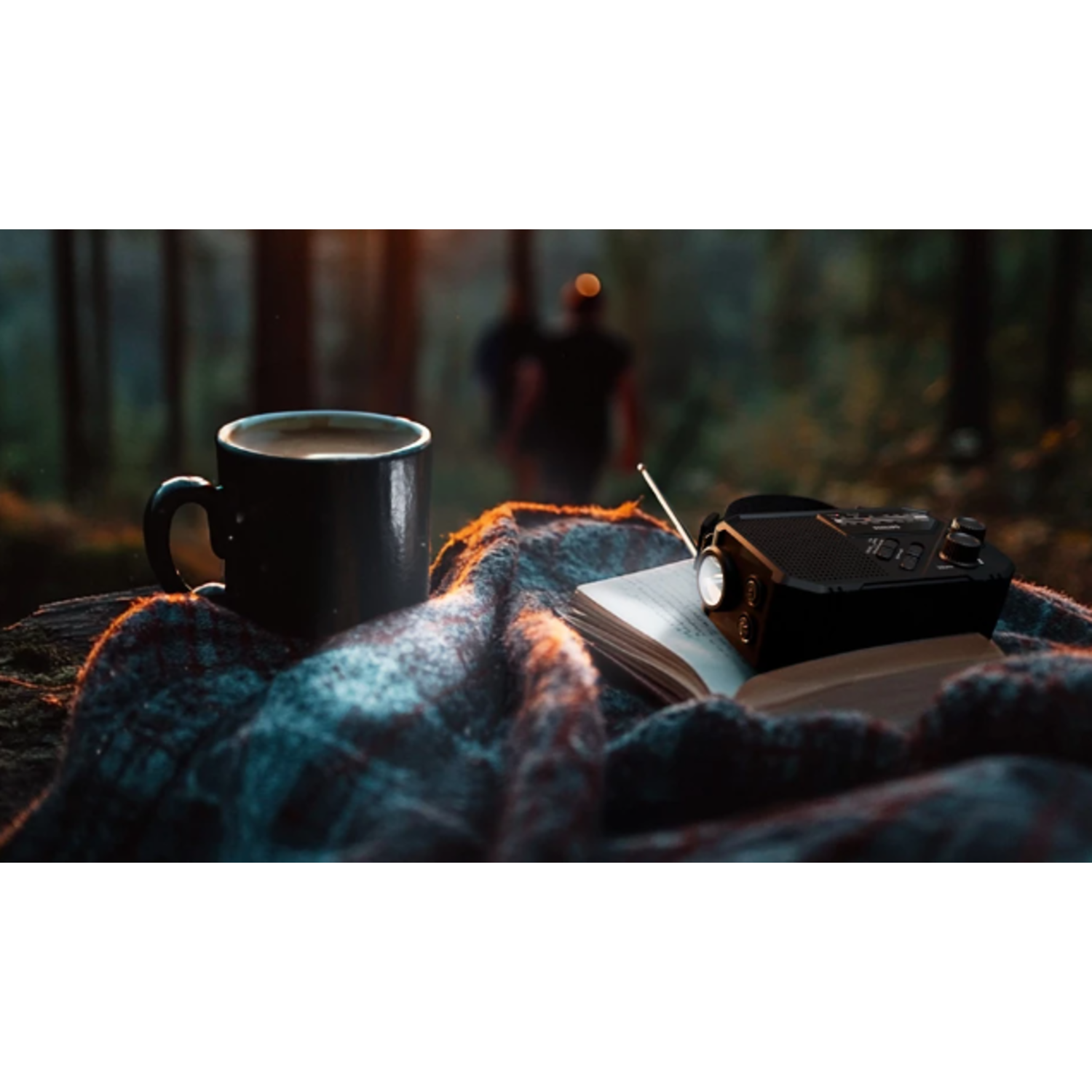 Een kop koffie, een boek en een radio op een geruite deken in een bos.