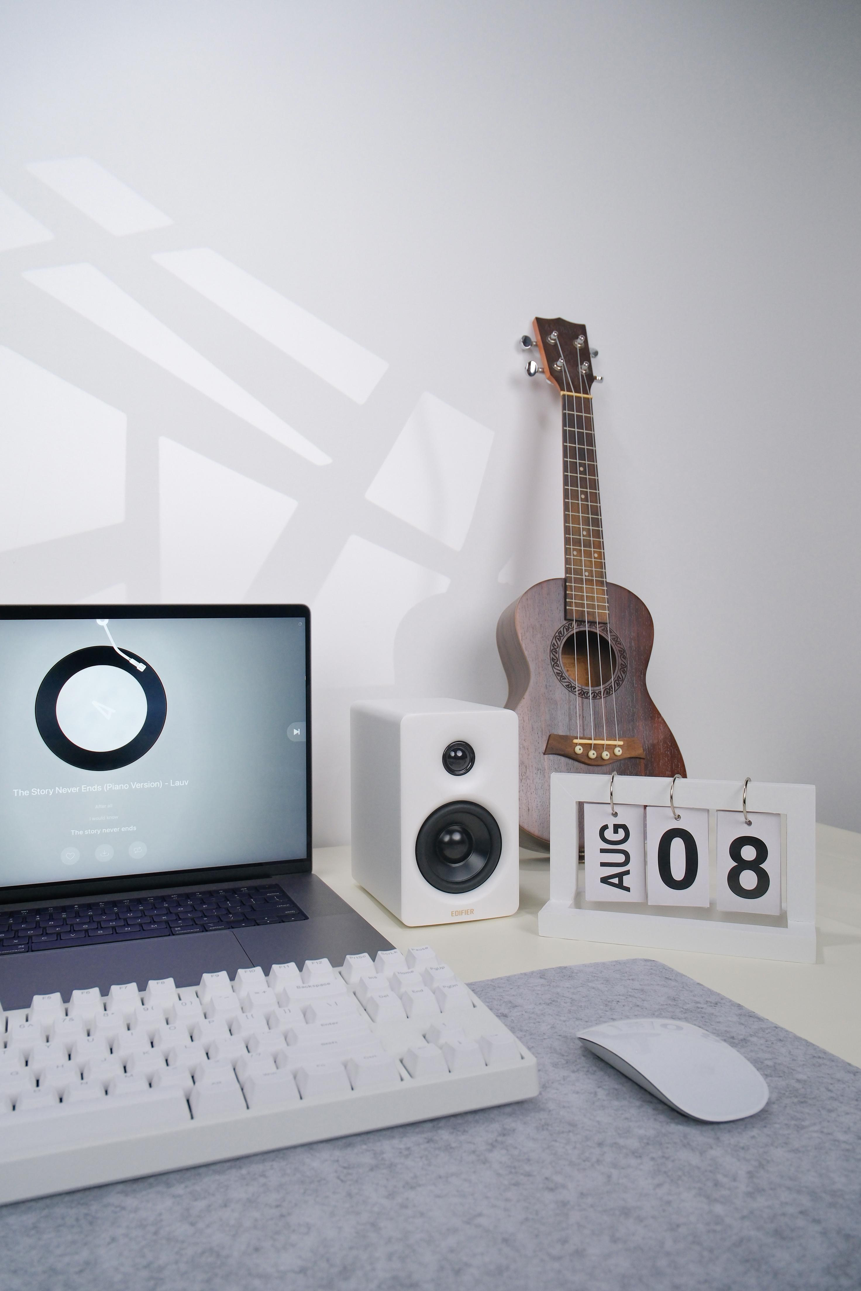 Ein Laptop mit einem Bildschirm, der einen Musikplayer, eine weiße Tastatur und eine Ukulele zeigt.