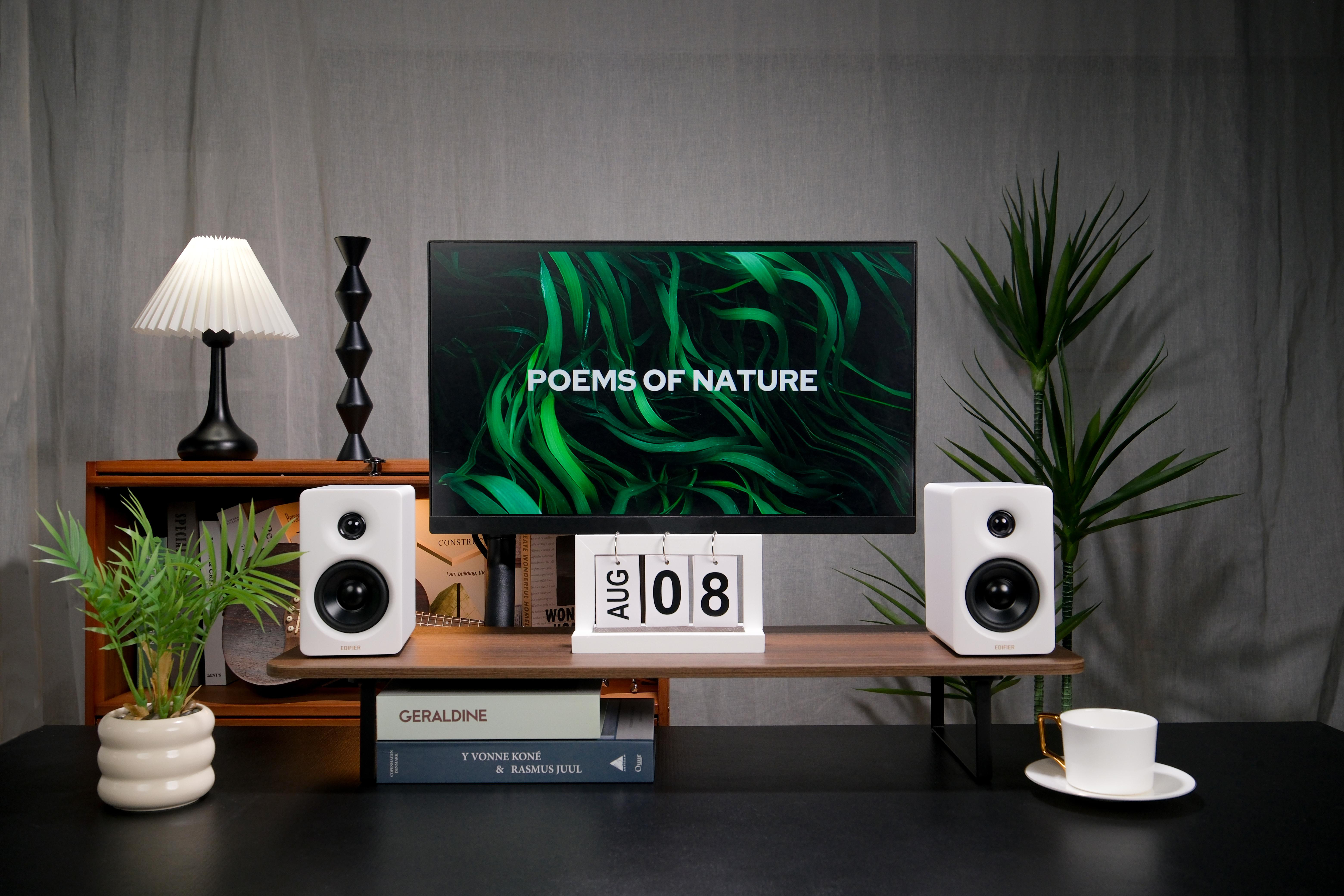 Ein Schreibtisch-Setup mit einem Monitor, der Text anzeigt, zwei weißen Lautsprechern und Deko.