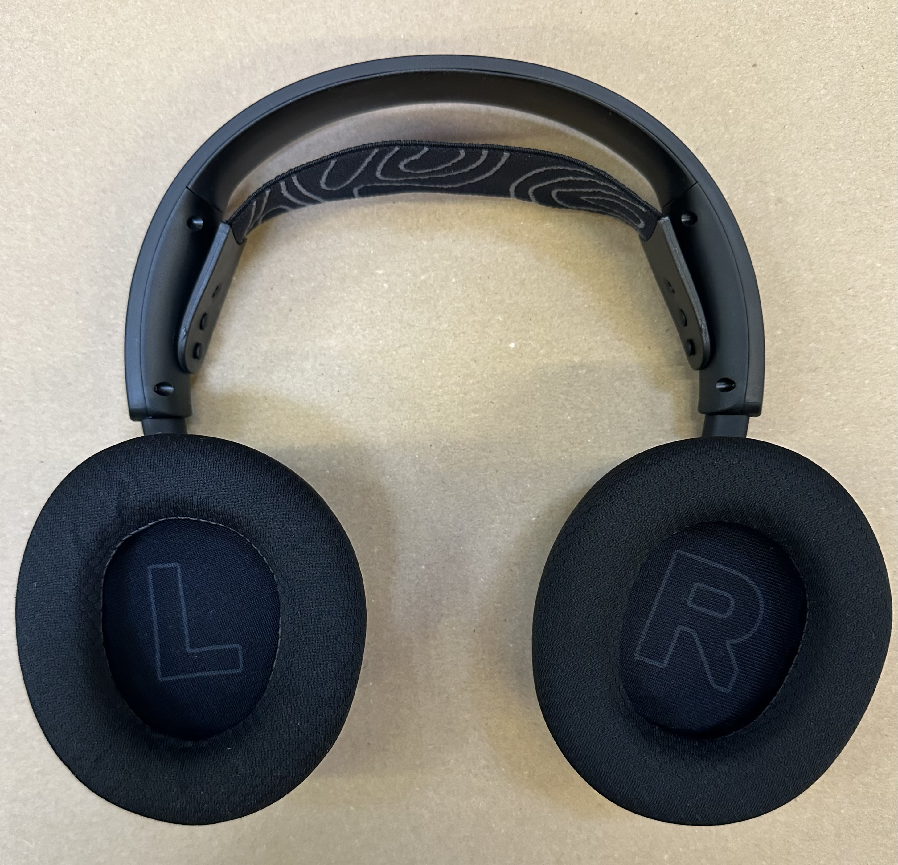 Czarne słuchawki z 'L' i 'R' na nausznikach, na beżowej powierzchni.