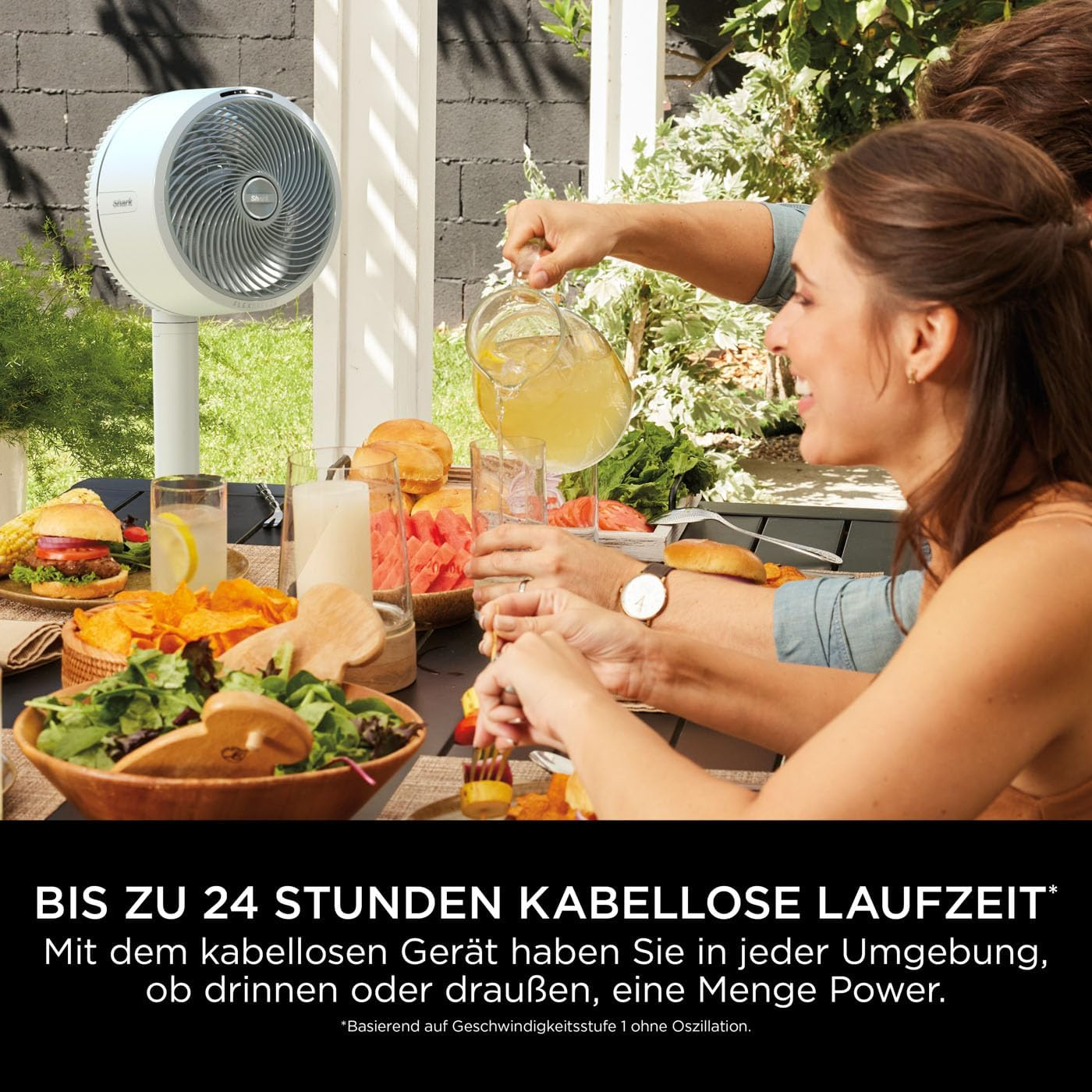 Persone a tavola con cibo, a cui viene servita limonata. C'è un ventilatore bianco nelle vicinanze. Hamburger, patatine, insalata sono sul tavolo.