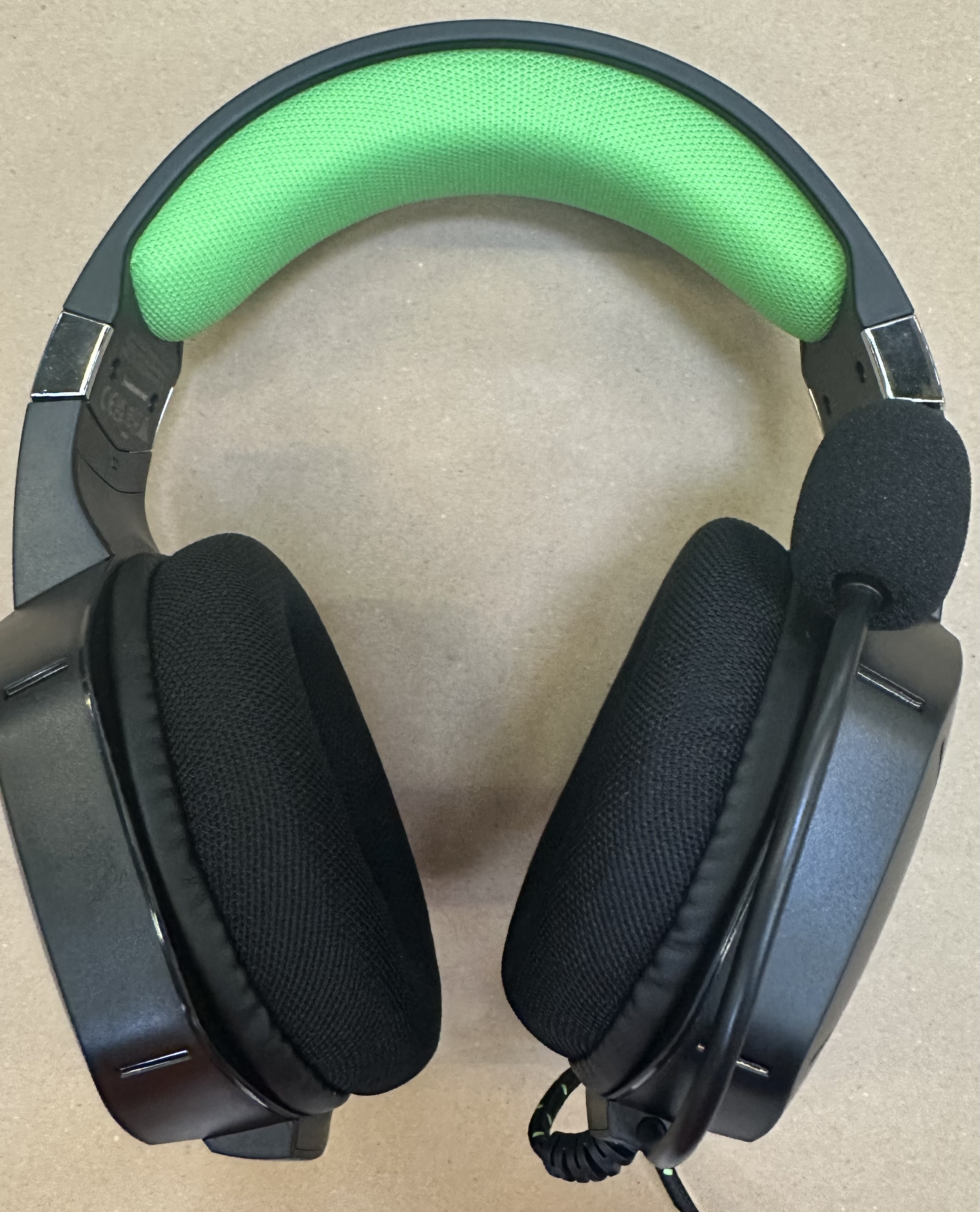 Czarne słuchawki dla graczy z zieloną poduszką na pałąku, na beżowej powierzchni.
