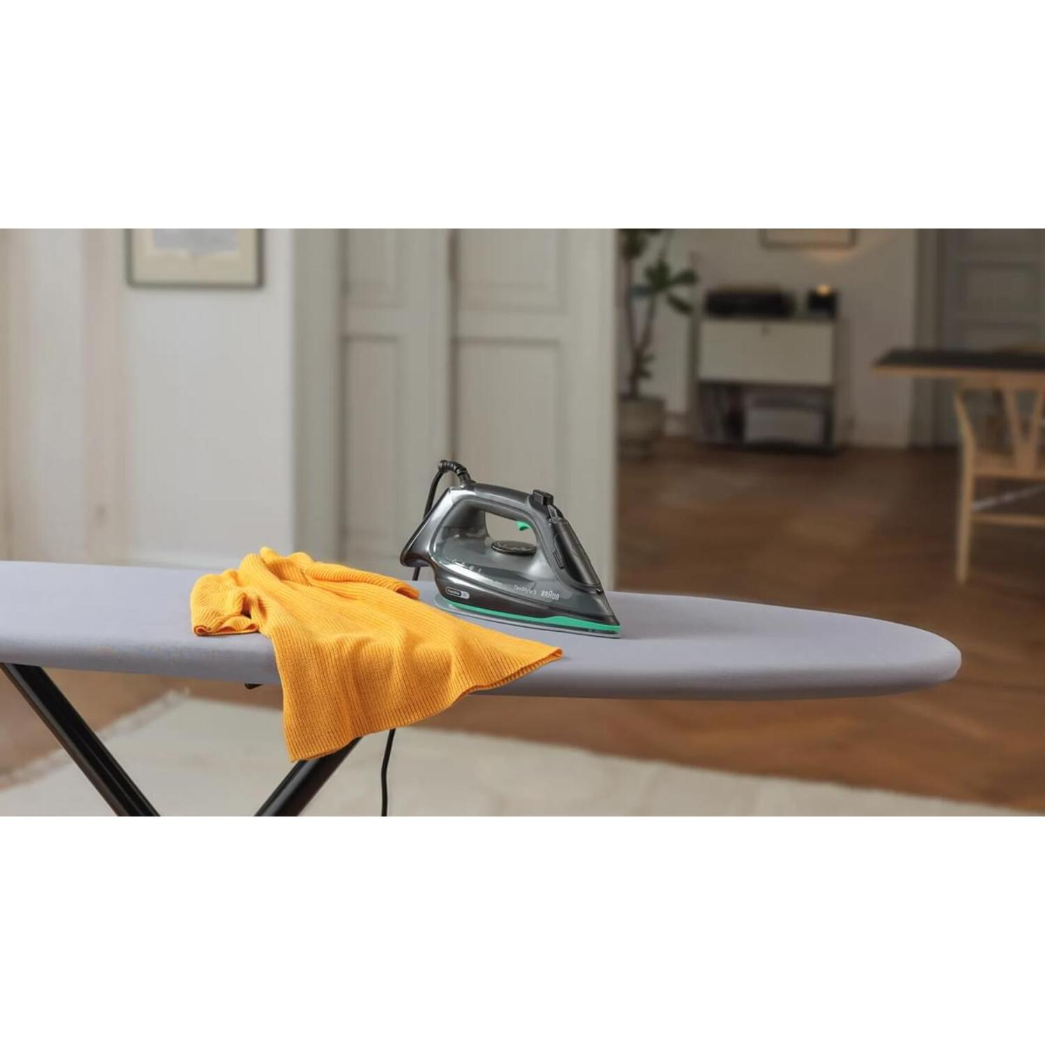 Un fer à repasser sur une planche à repasser grise avec un tissu jaune dans un cadre domestique.