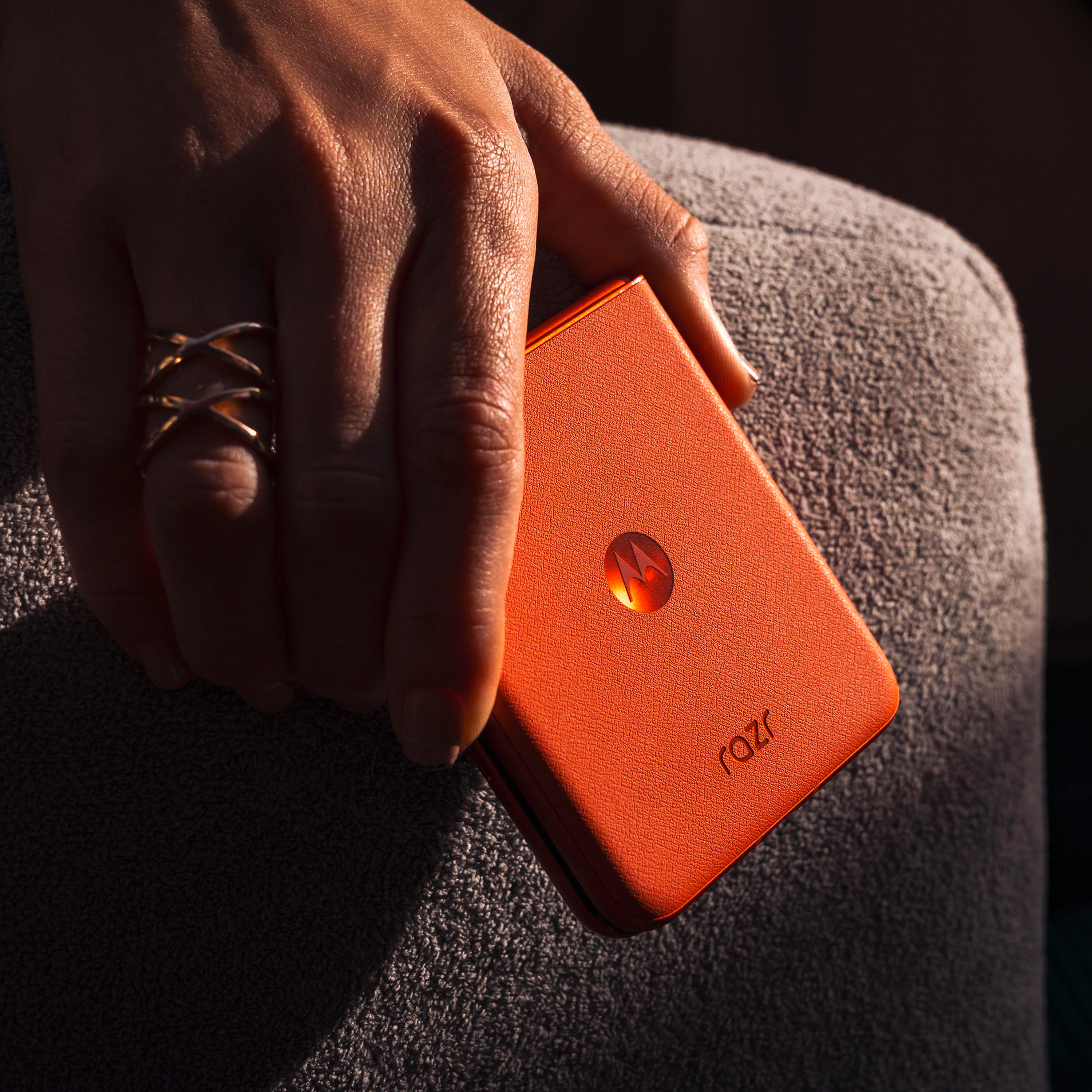 Hand hält geschlossenes orangefarbenes Motorola Razr 50 Telefon, Ring am Finger.