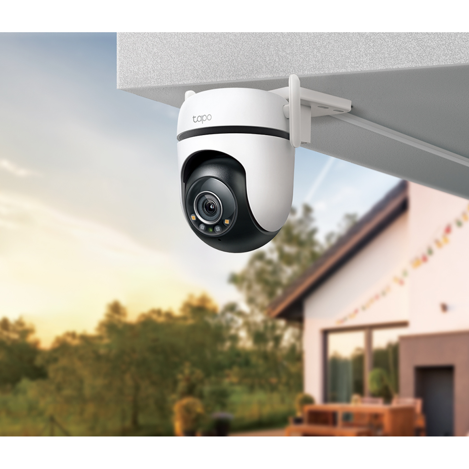 Tapo camera gemonteerd onder een dak. Huis en bomen zijn wazig op de achtergrond.