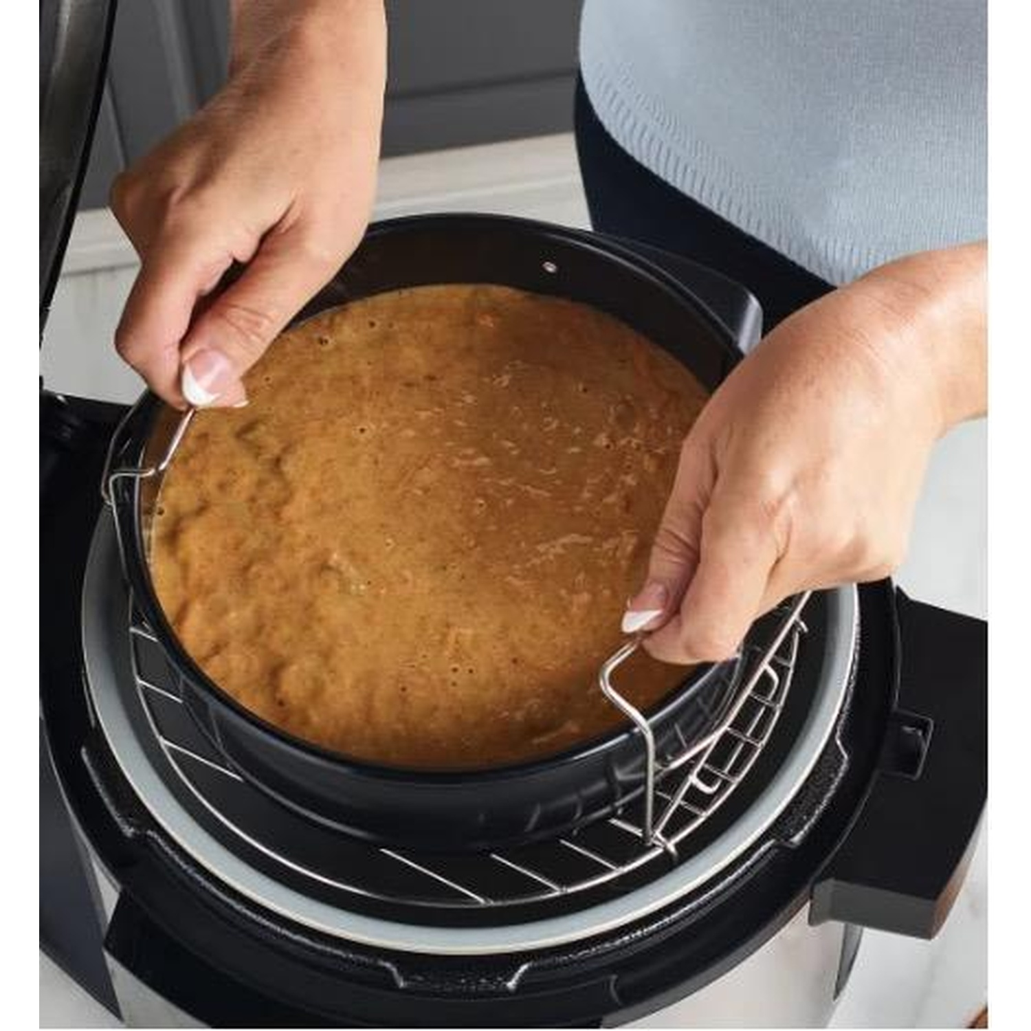 Le mani di un uomo tengono una tortiera nera con pastella all'interno di una pentola a pressione.