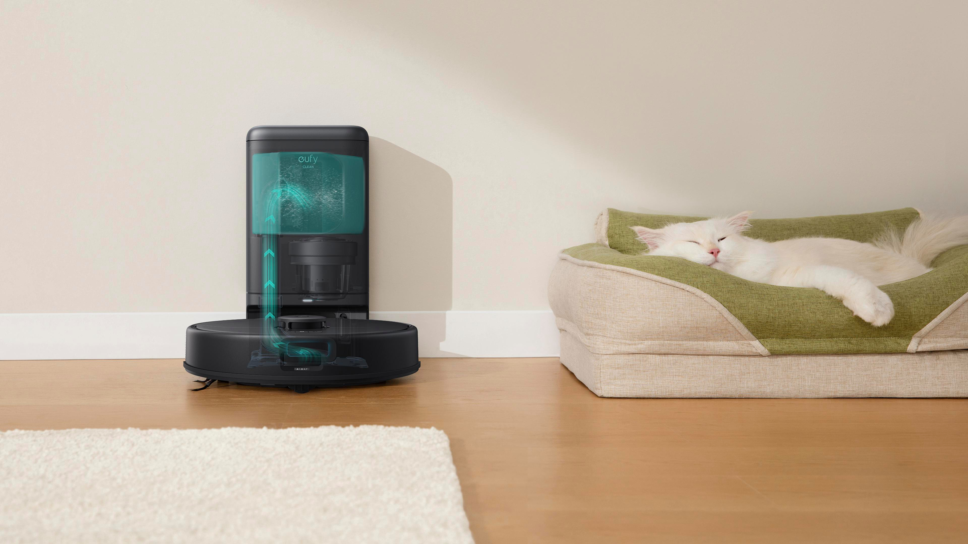 Ein Roboter-Staubsauger und eine schlafende weiße Katze in einem grünen Bett. Der Staubsauger ist schwarz mit tealfarbenen Akzenten.