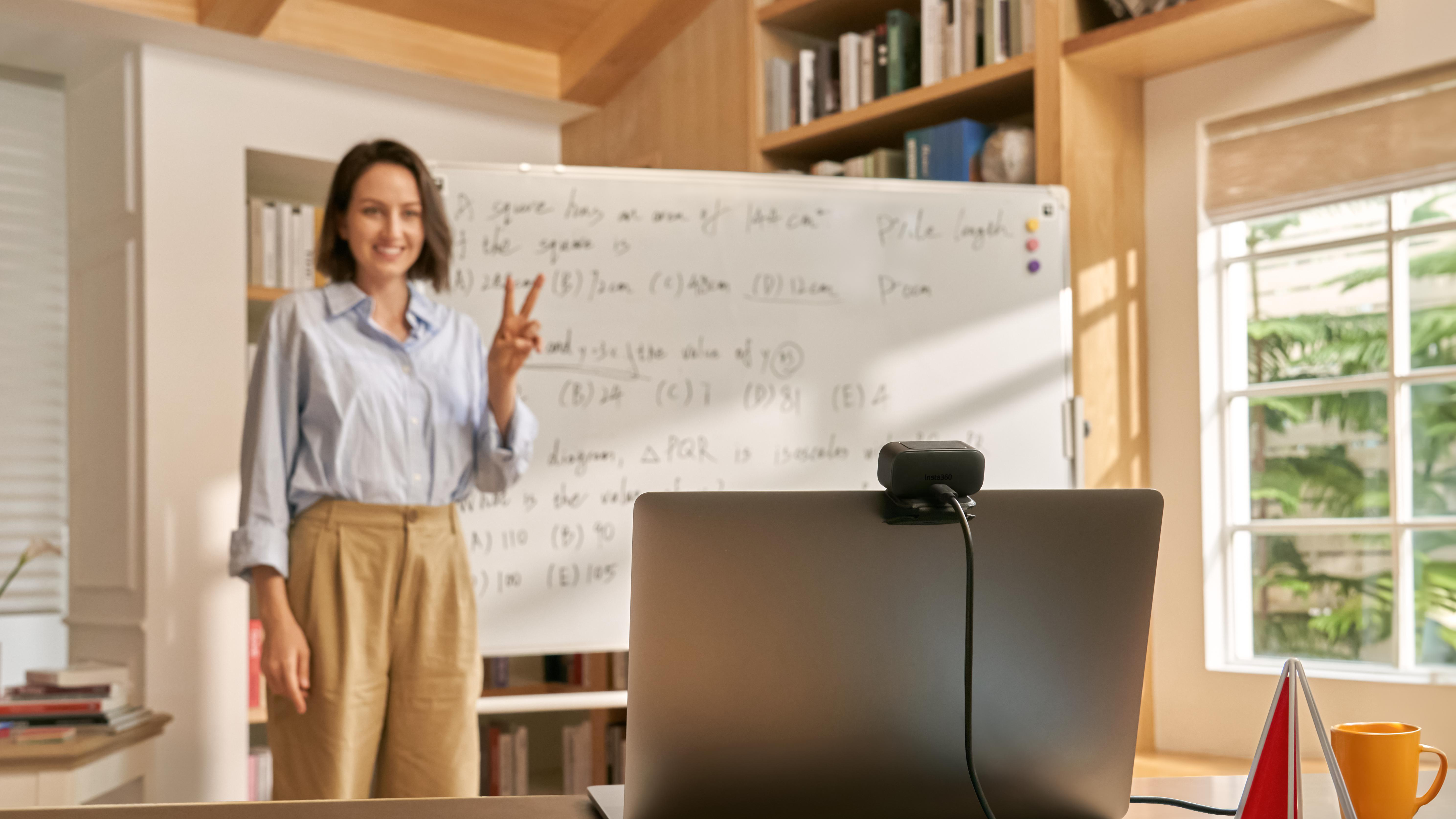 Frau vor Whiteboard, Friedenszeichen, Webcam auf Laptop.