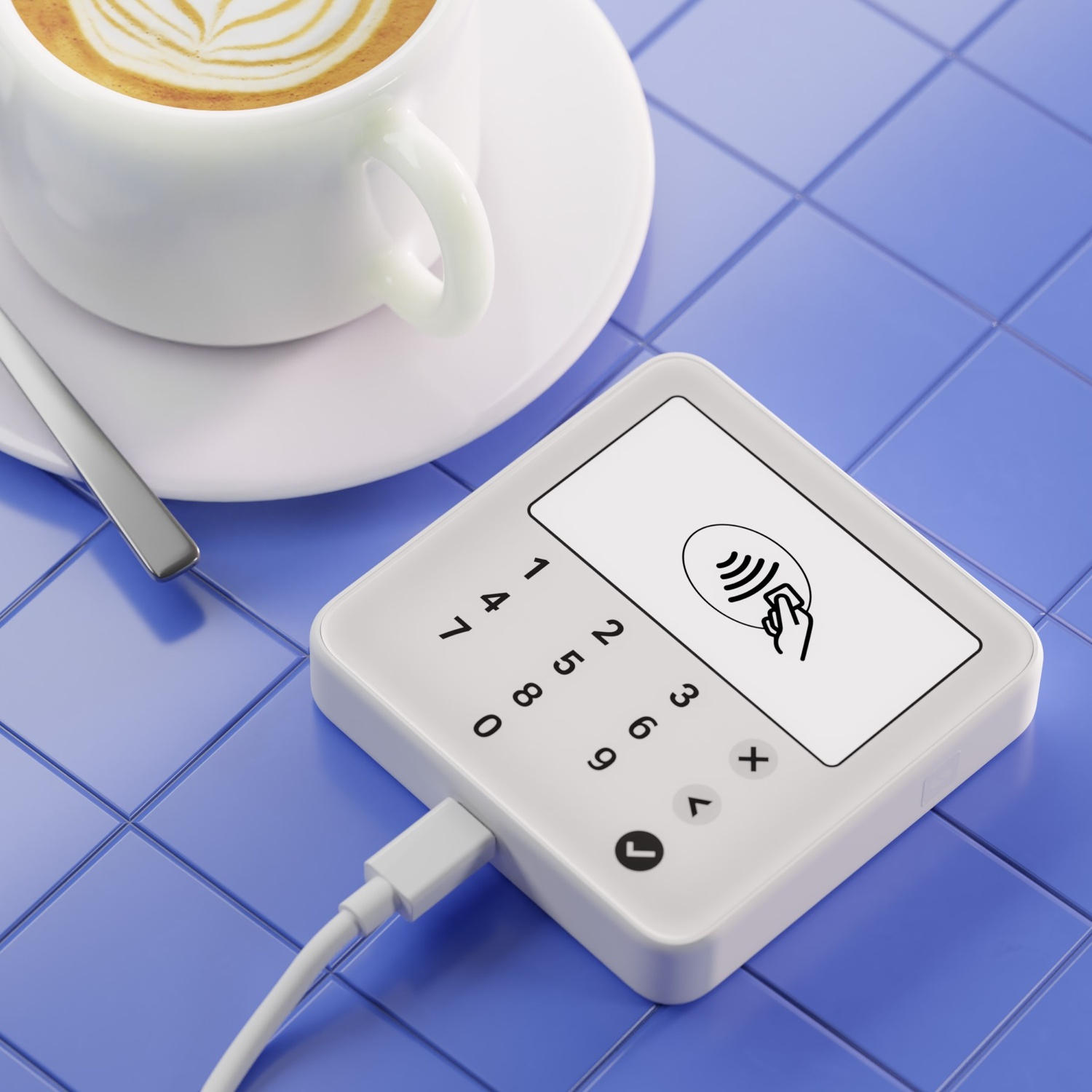 Un terminale di pagamento bianco con numeri e schermo, un caffè e un cucchiaio su piastrelle blu.